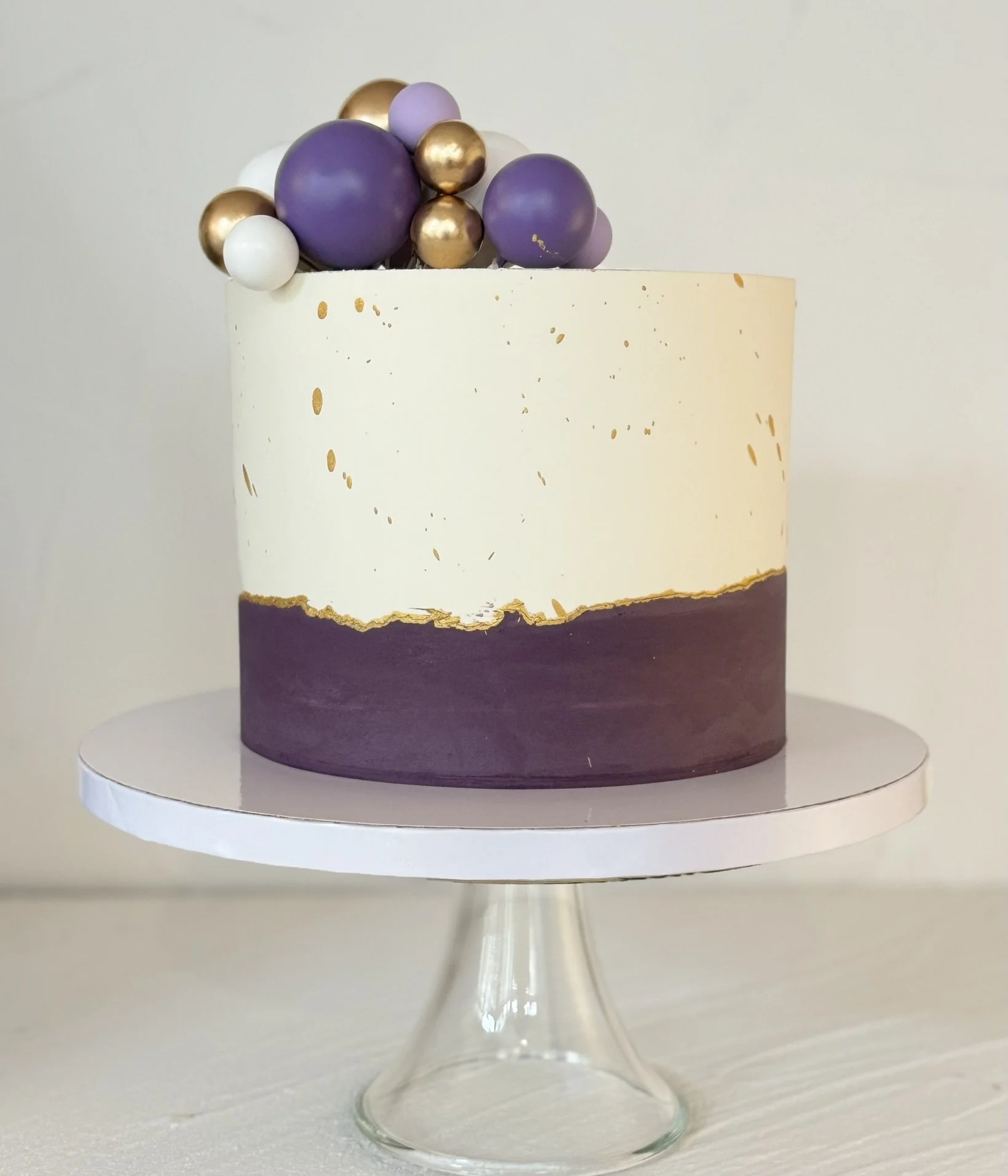 White and purple cake with purple and gold spherical toppers.