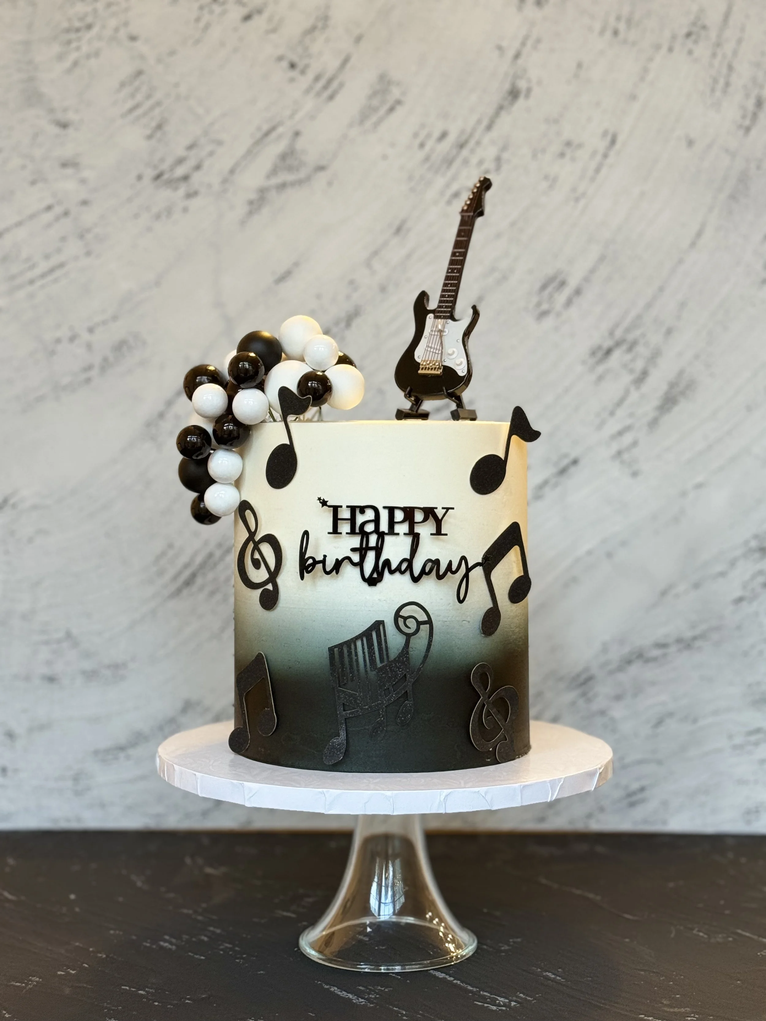 Black and white cake decorated with musical notes and a guitar topper.
