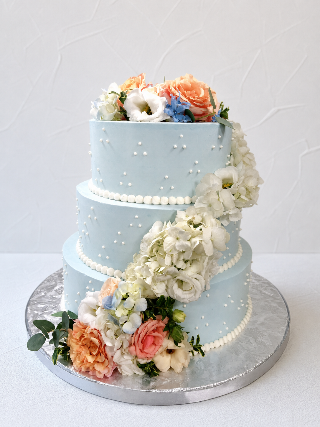 Pale blue tiered cake with peach flowers and a cascade of white floral decoration.