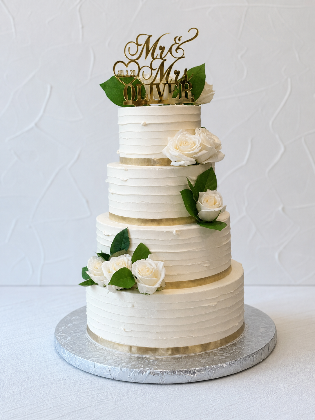 White tiered cake with horizontal bands, green leaves, and pale flowers.