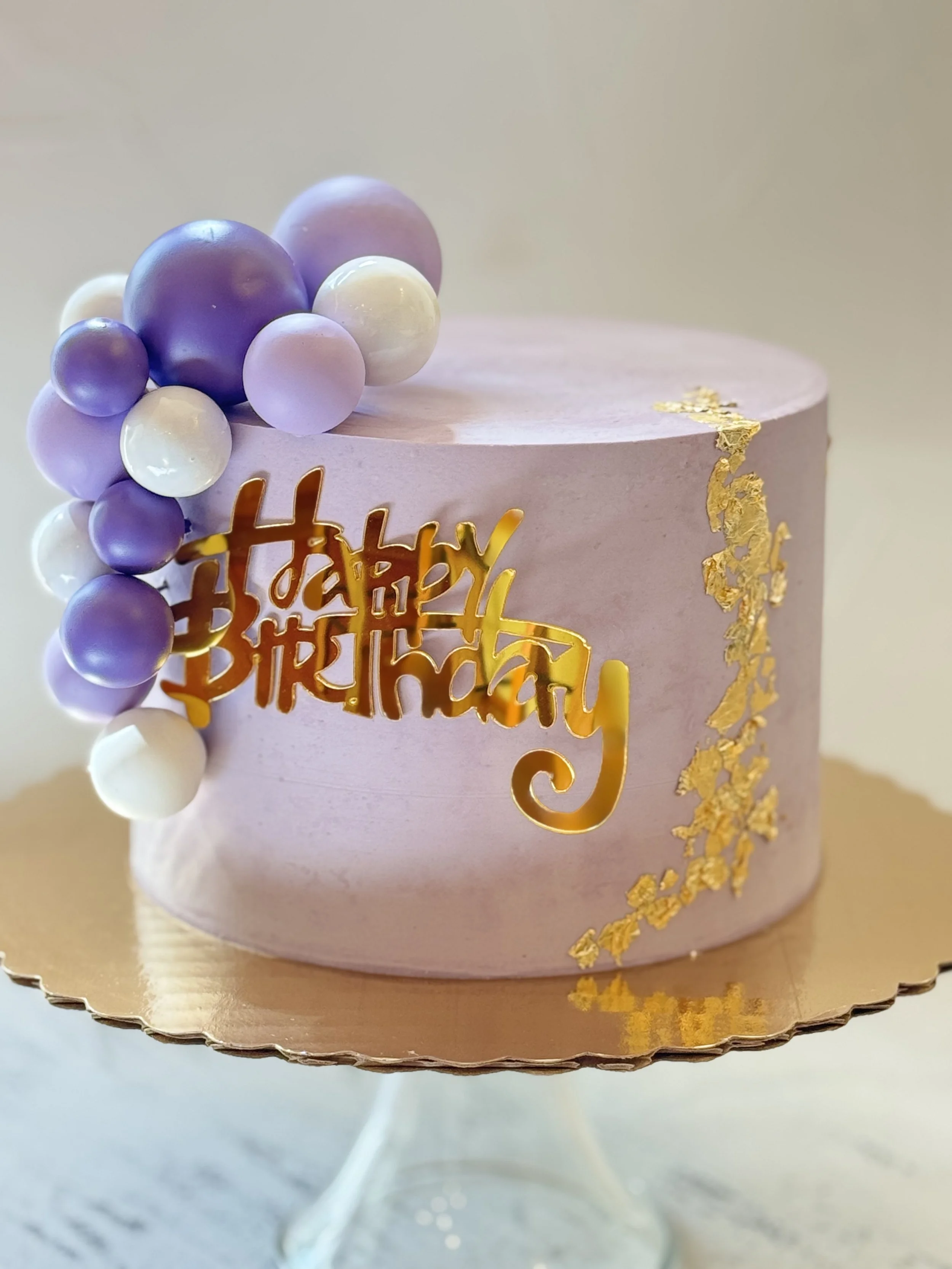 Lavender cake with purple and white balloon-like decorations and gold accents.