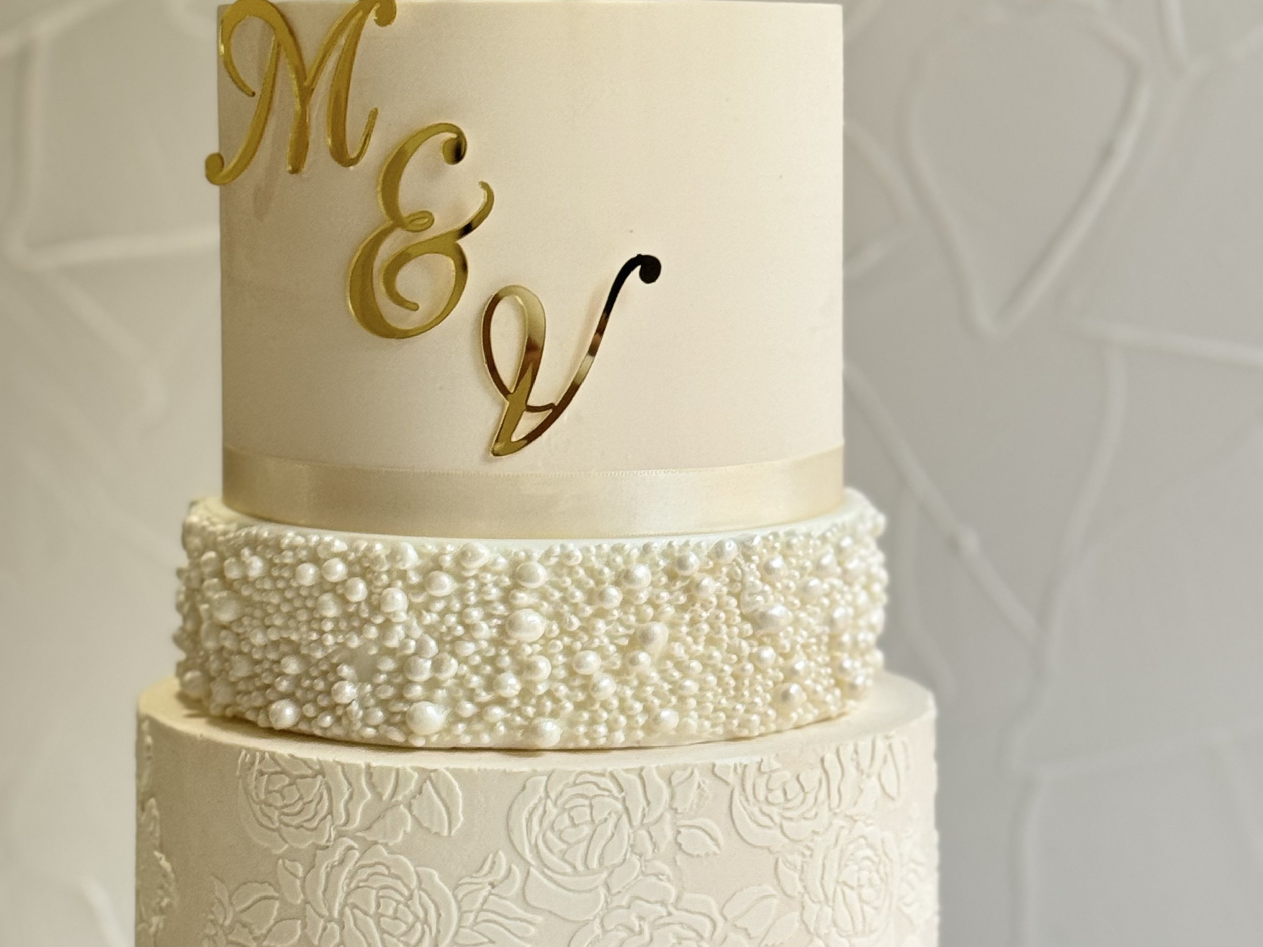 Close-up of a white cake with gold initials and a textured gold band.