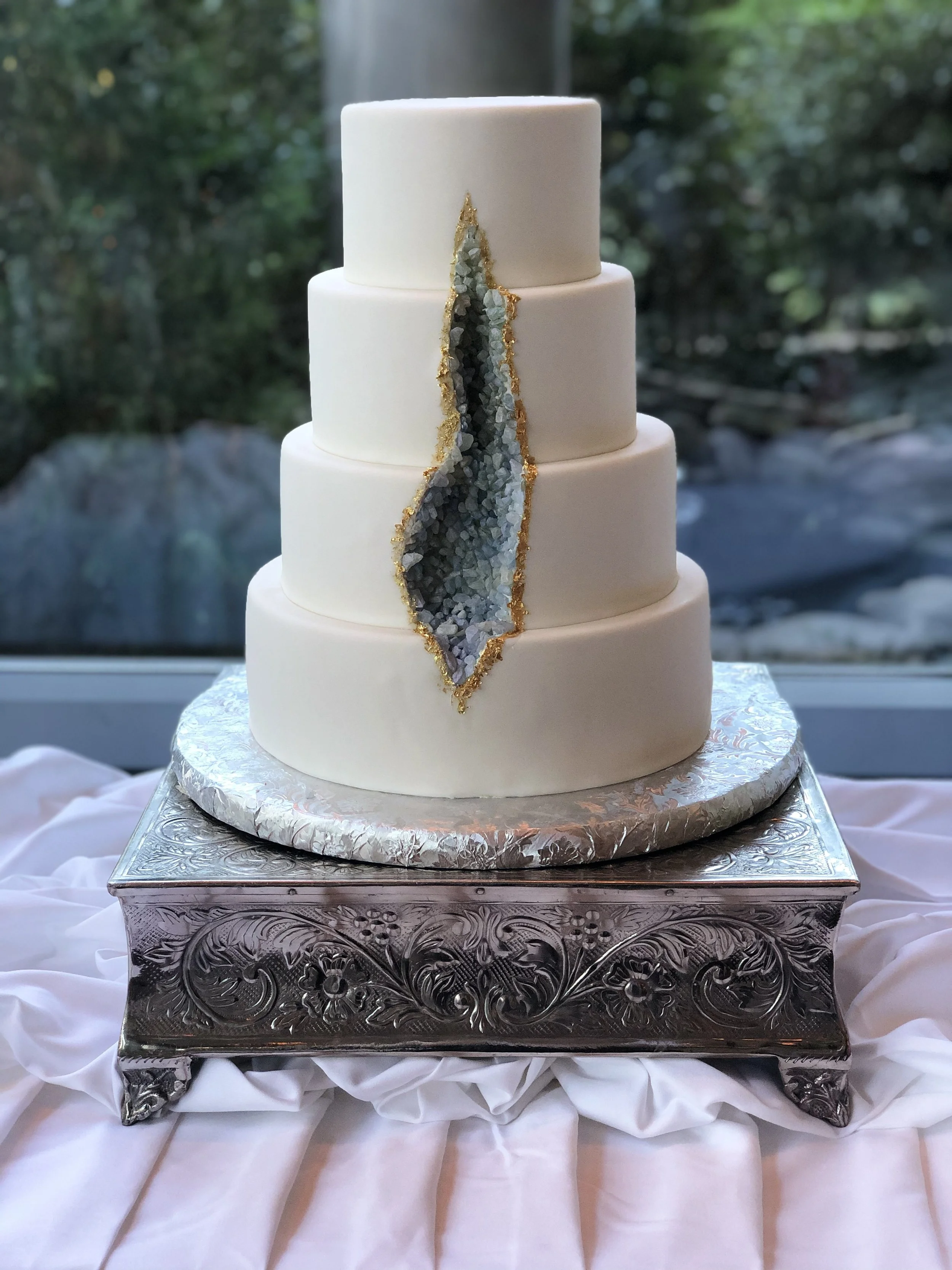 Tiered cake with white and taupe panels and a vertical trail of green leaves.