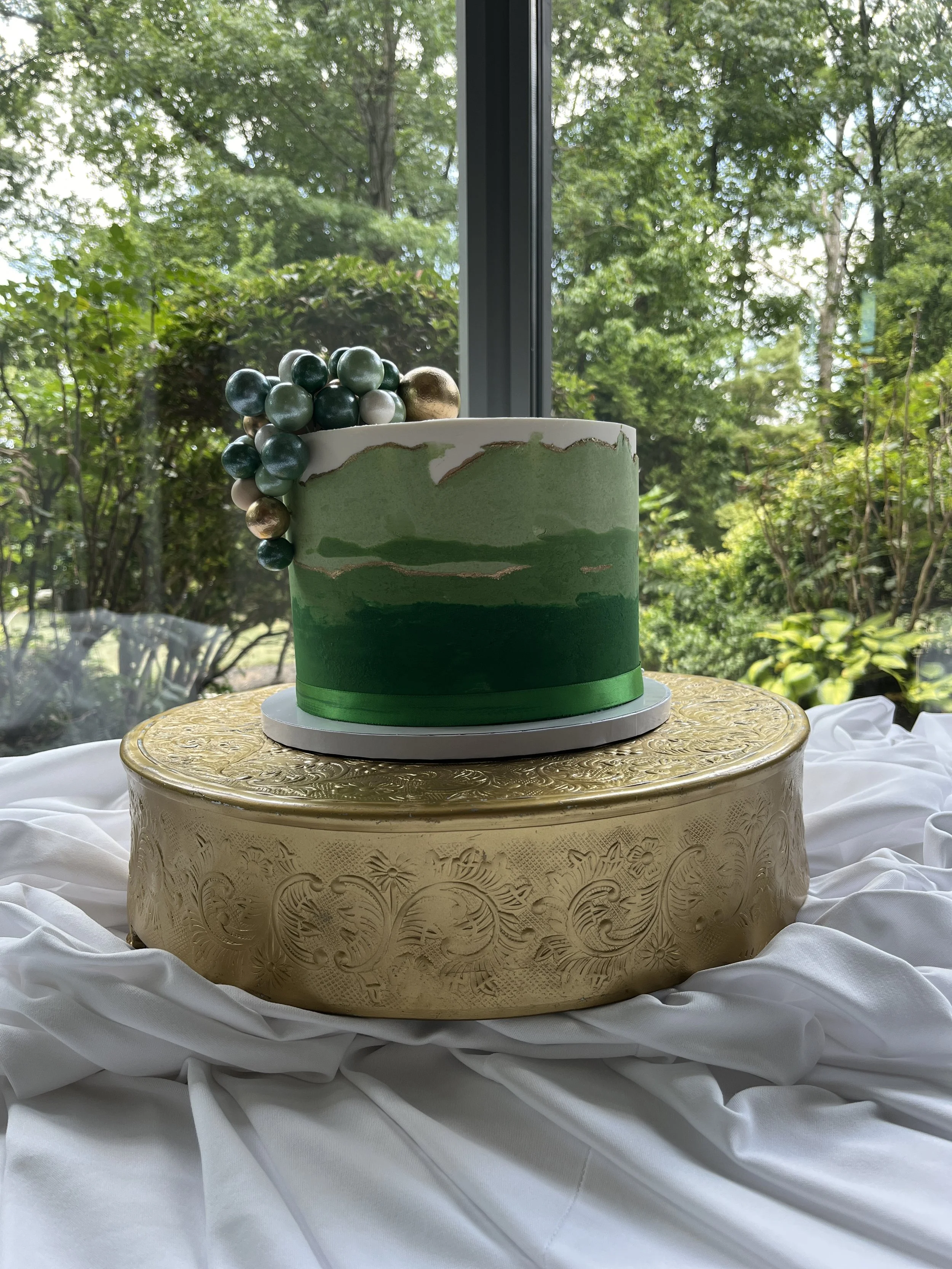 Dark green cake displayed outdoors on a wooden stand.