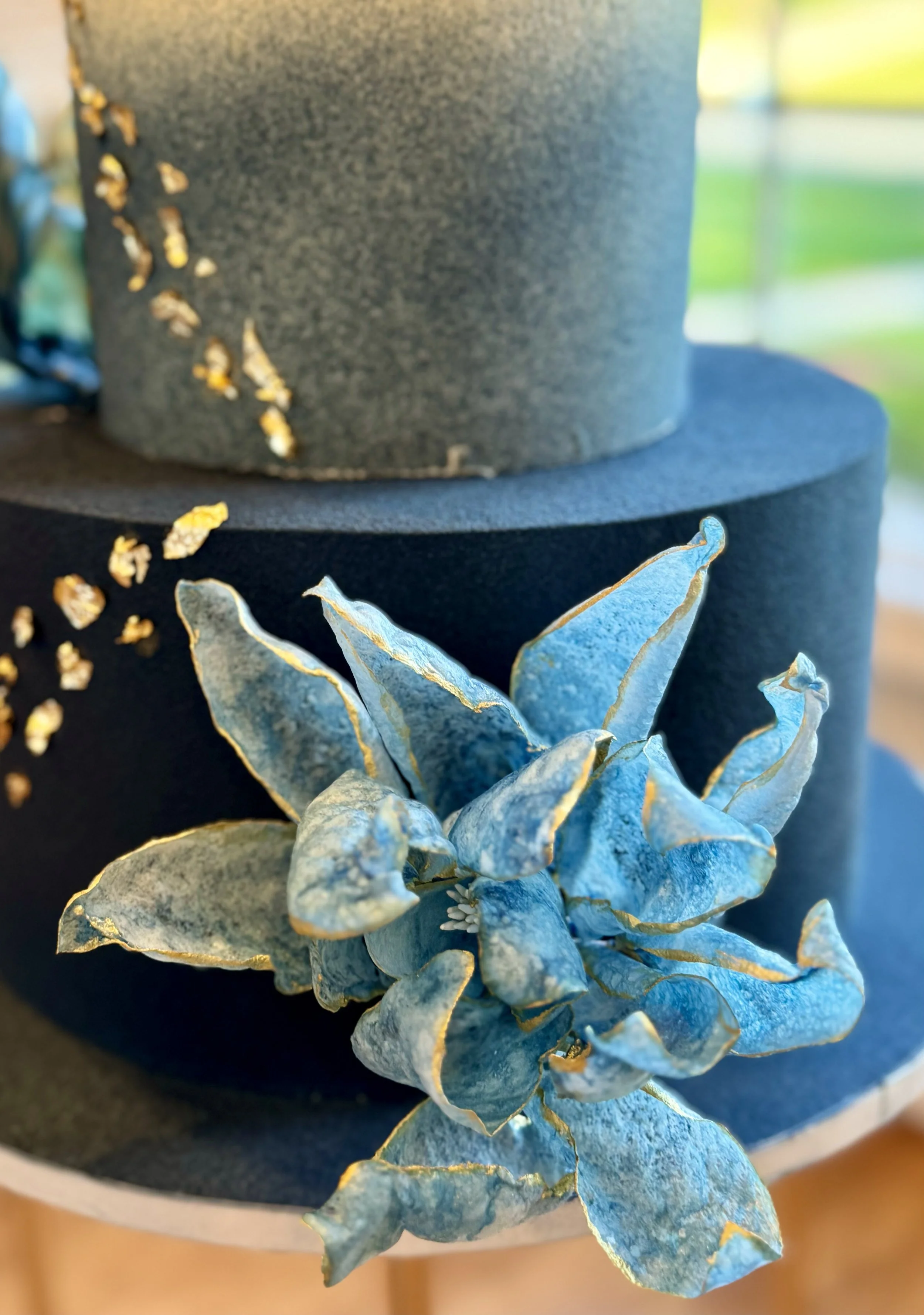 Close-up of a navy and gold cake with bright blue floral decoration.