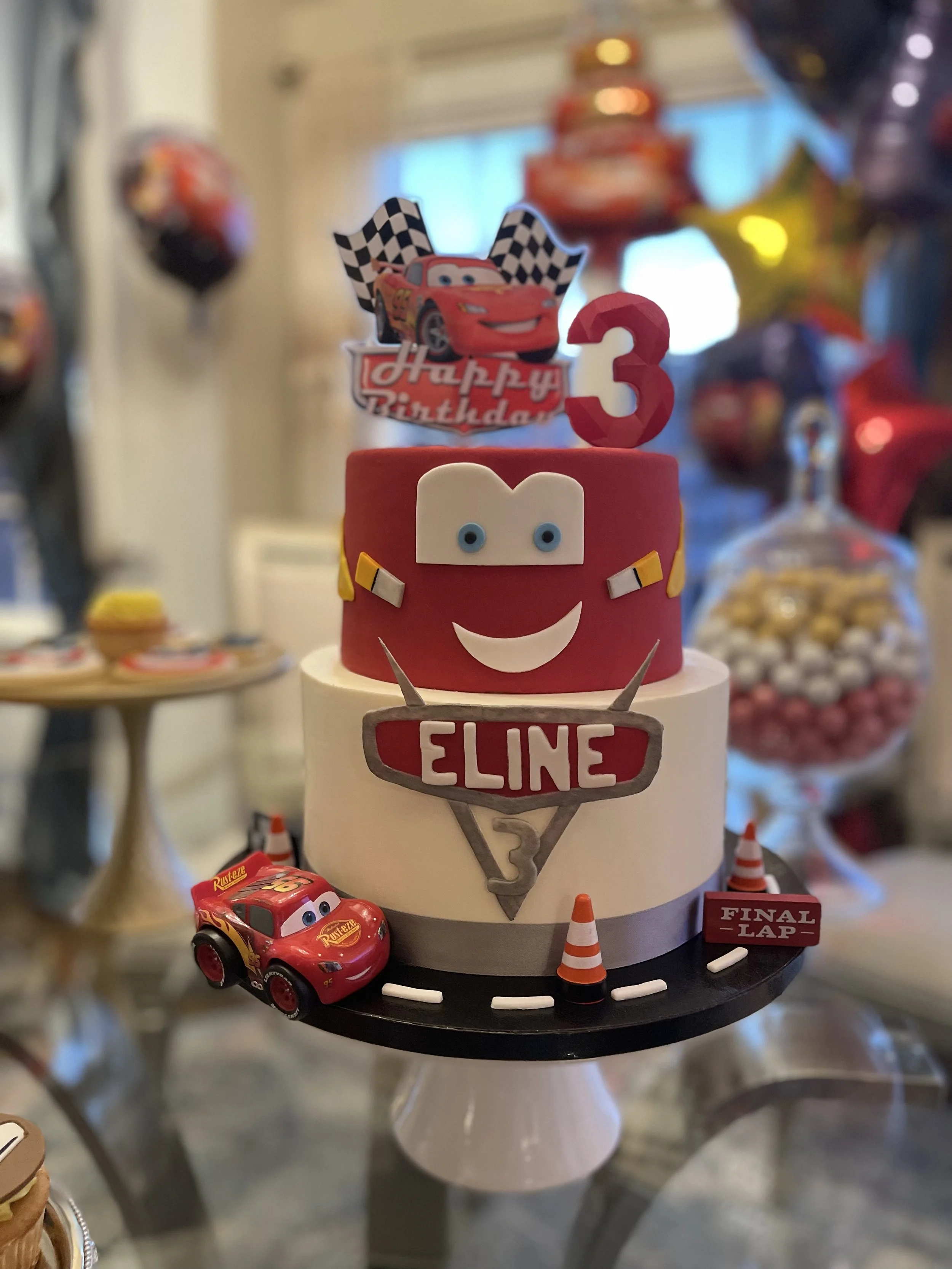 Red tiered cake with racing-car decorations and a number 3 topper.