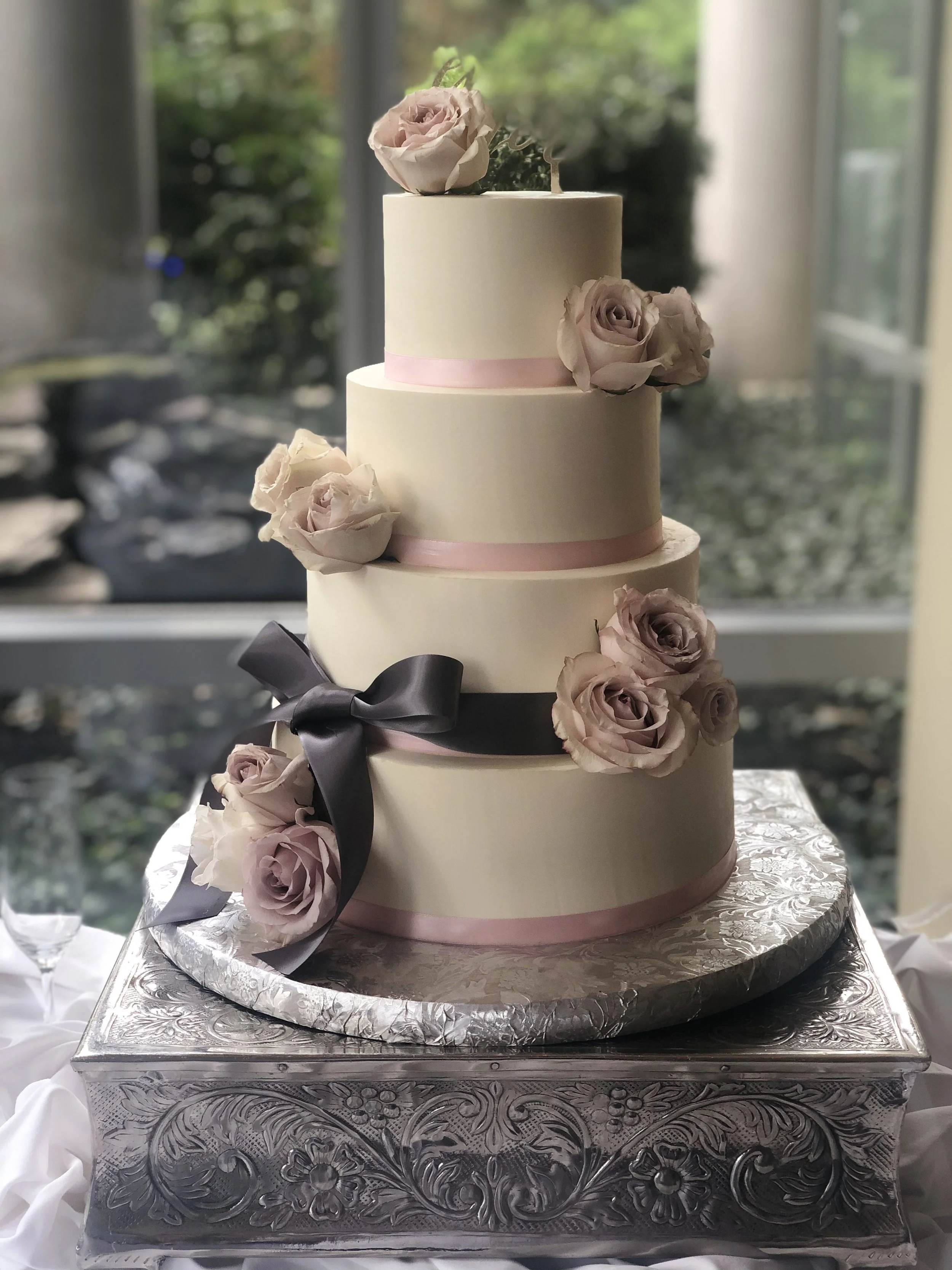 Taupe tiered cake with dark ribbon and pale pink flowers.