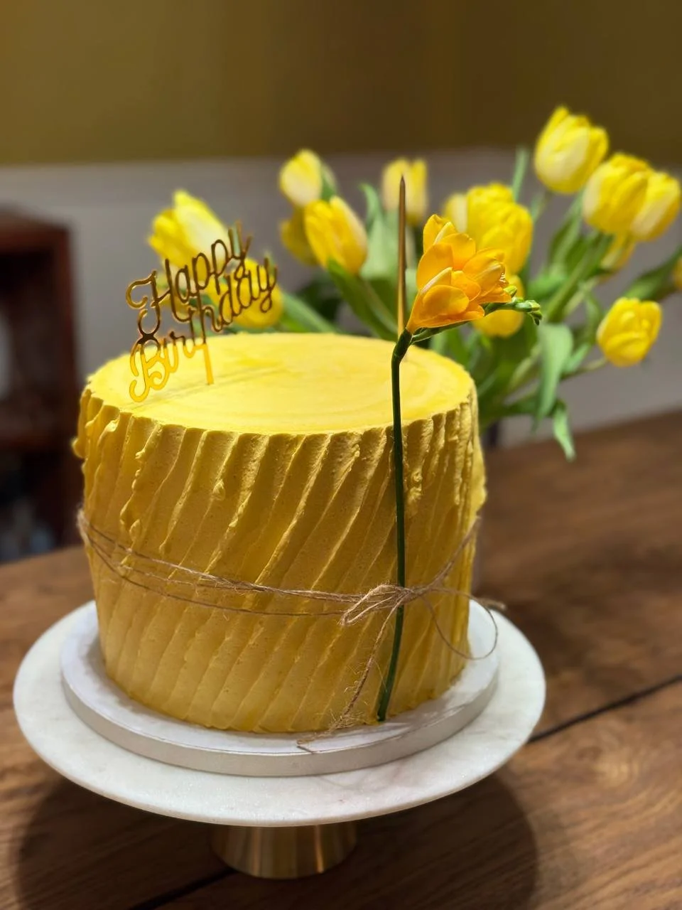Yellow cake with textured icing displayed in front of yellow tulips.