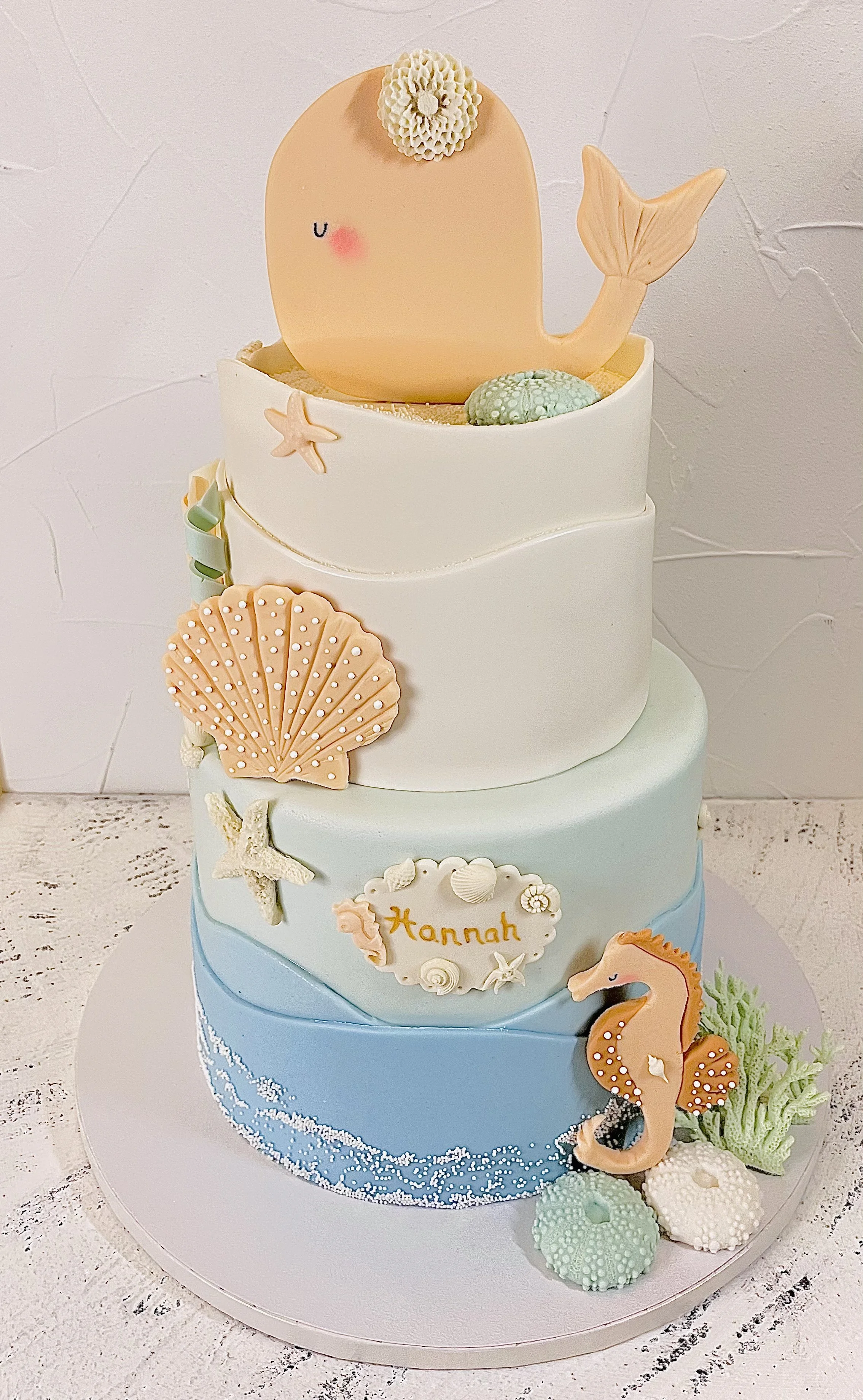 White and pale blue tiered cake with seashell and seahorse decorations.