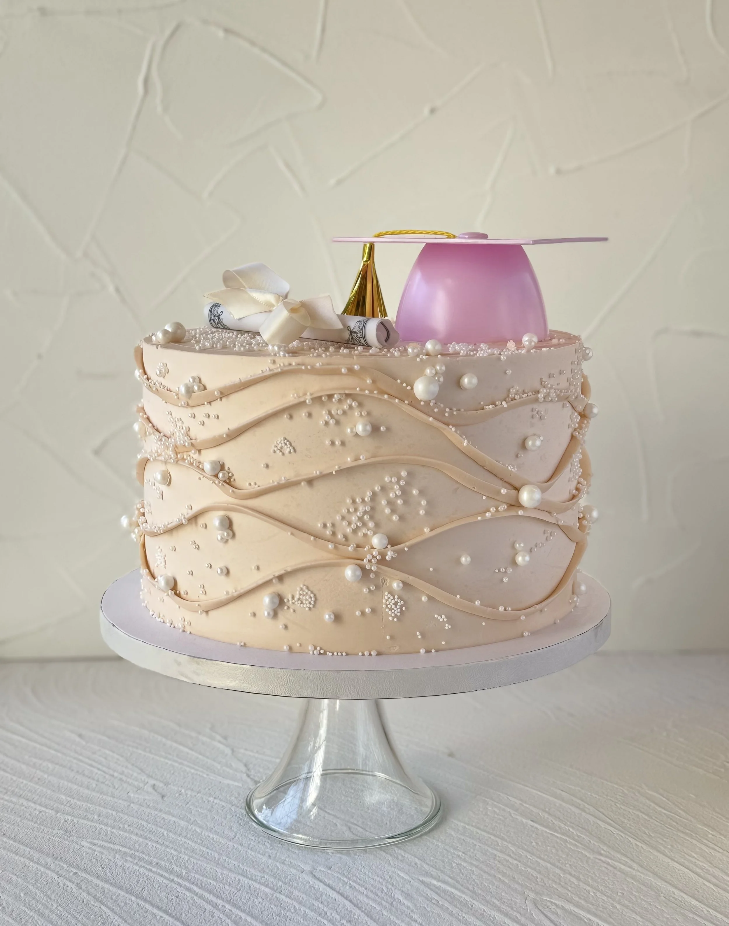 Pale pink cake with quilted-style decoration, pearl-like dots, and gold accents.