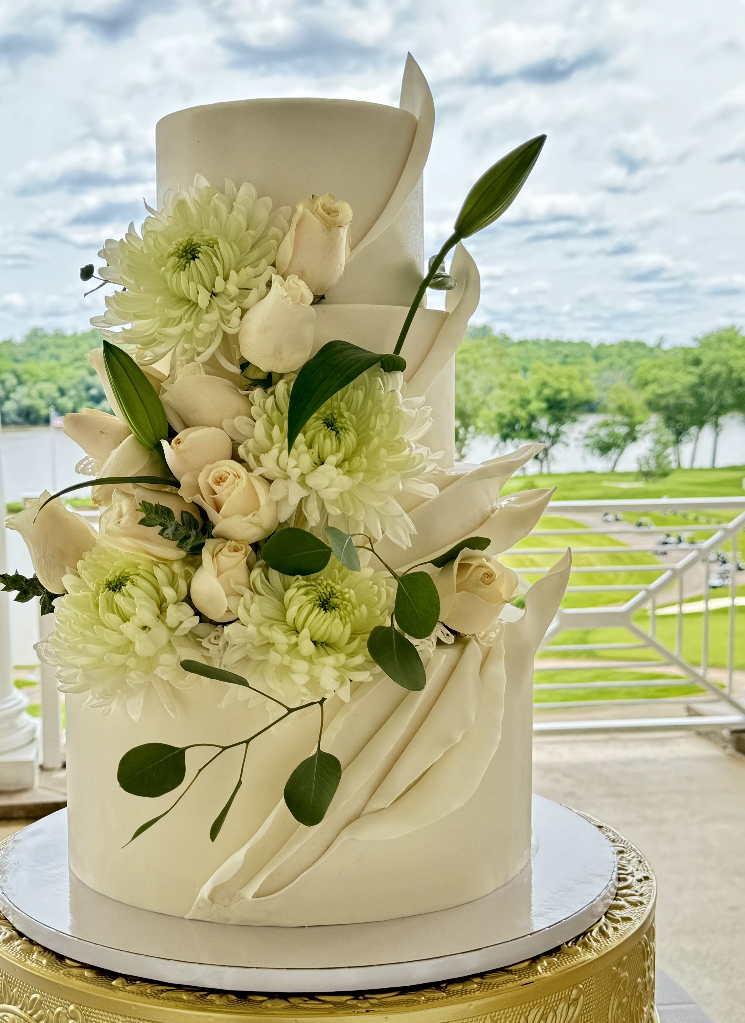 White cake decorated with a cascade of white flowers and green leaves.