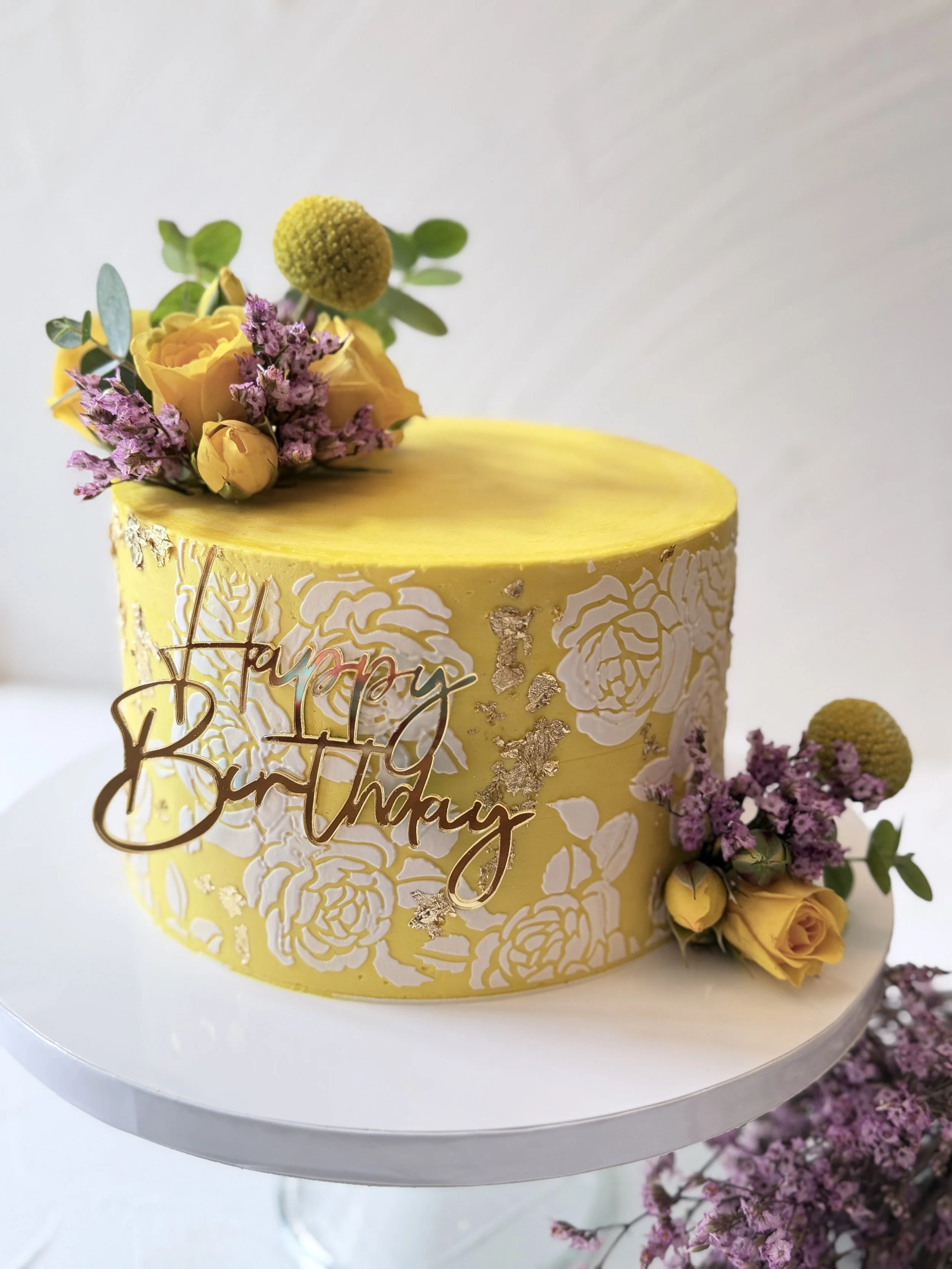 White and yellow cake with gold details and flowers.