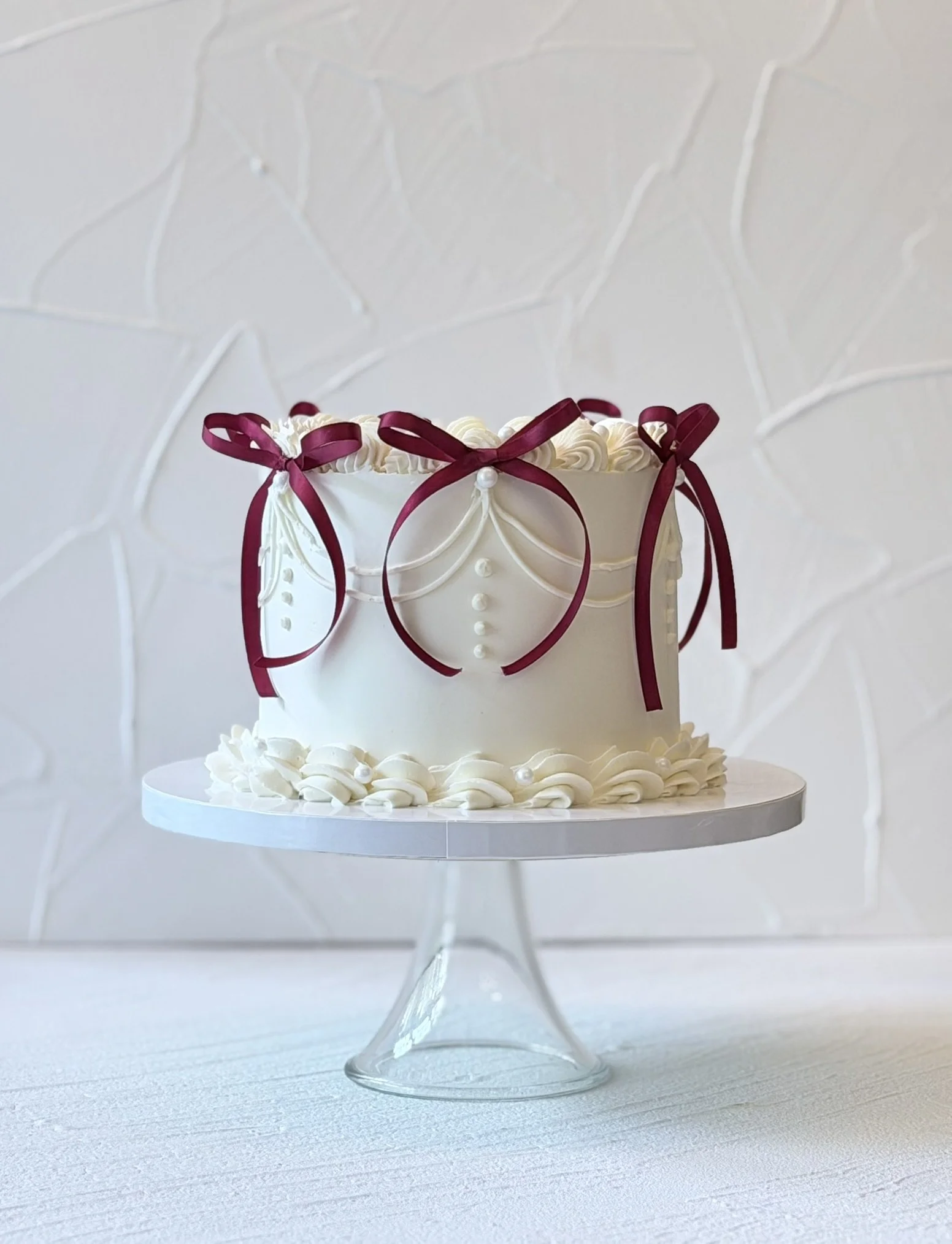 White cake with burgundy bows and draped pearl-like decoration.
