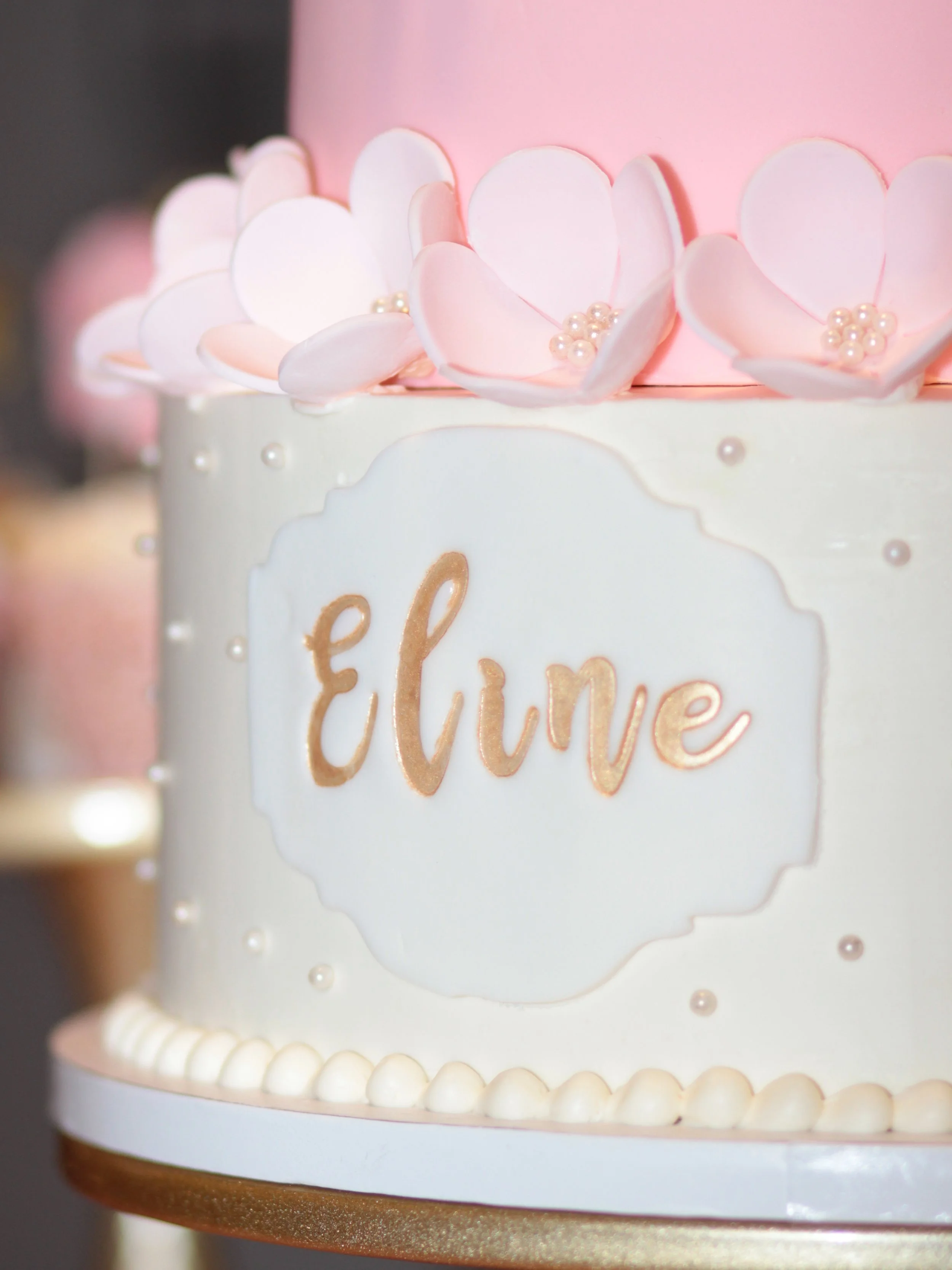 White cake with gold script and pink balloon-like decorations.