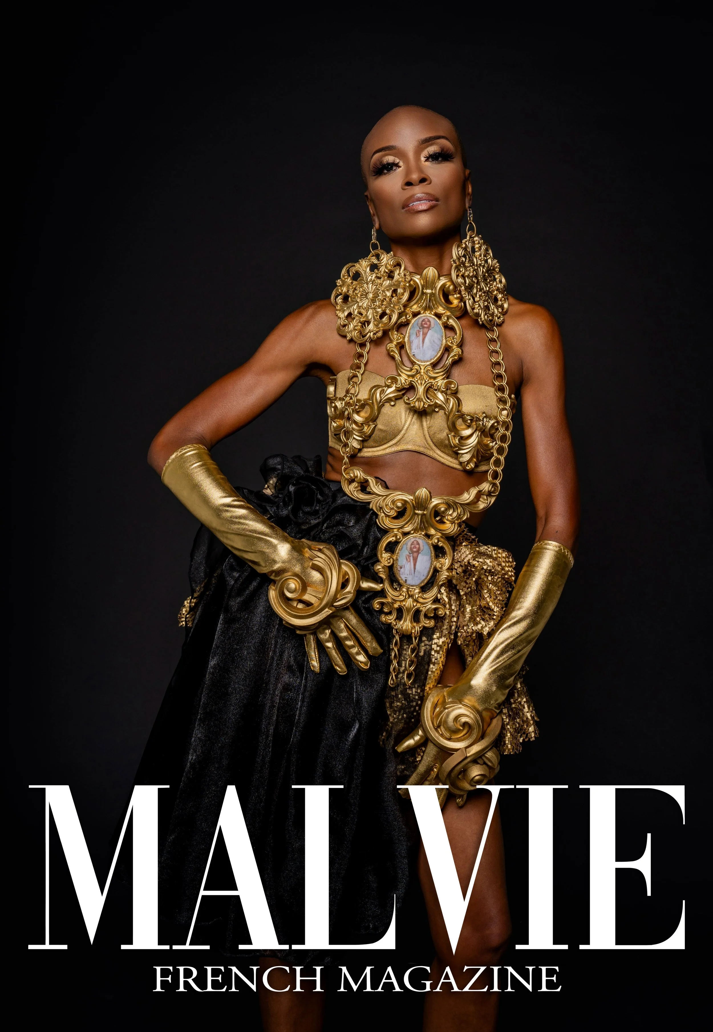 A woman with dark skin and a shaved head wearing gold jewelry and gold gloves, posing against a black background with the words 'MADELINE FRENCH MAGAZINE' at the bottom.