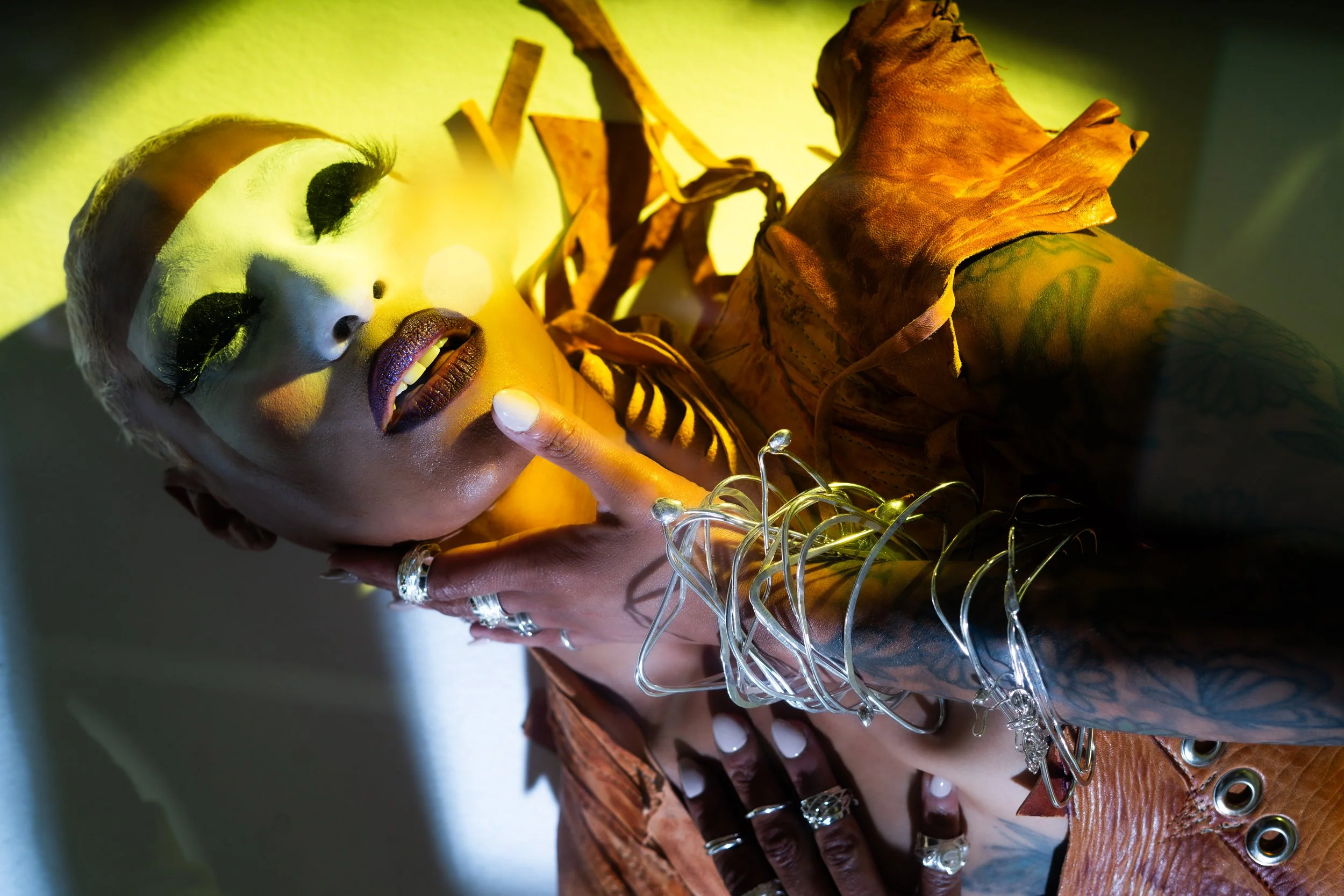 Close-up of a doll with makeup, surrounded by dried leaves, jewelry, and decorative lights in a warm, yellow-green glow.