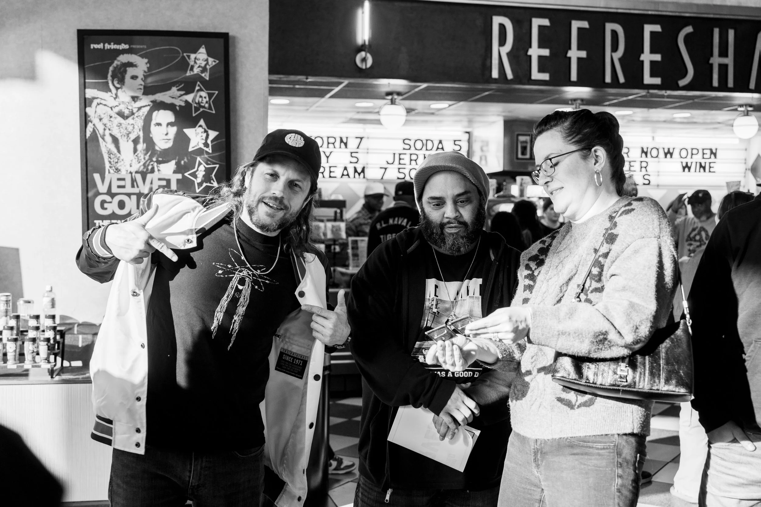 Three people standing in a busy indoor space, one of them showing a card to the woman on the right, with a sign that says "RETREAT" above them.