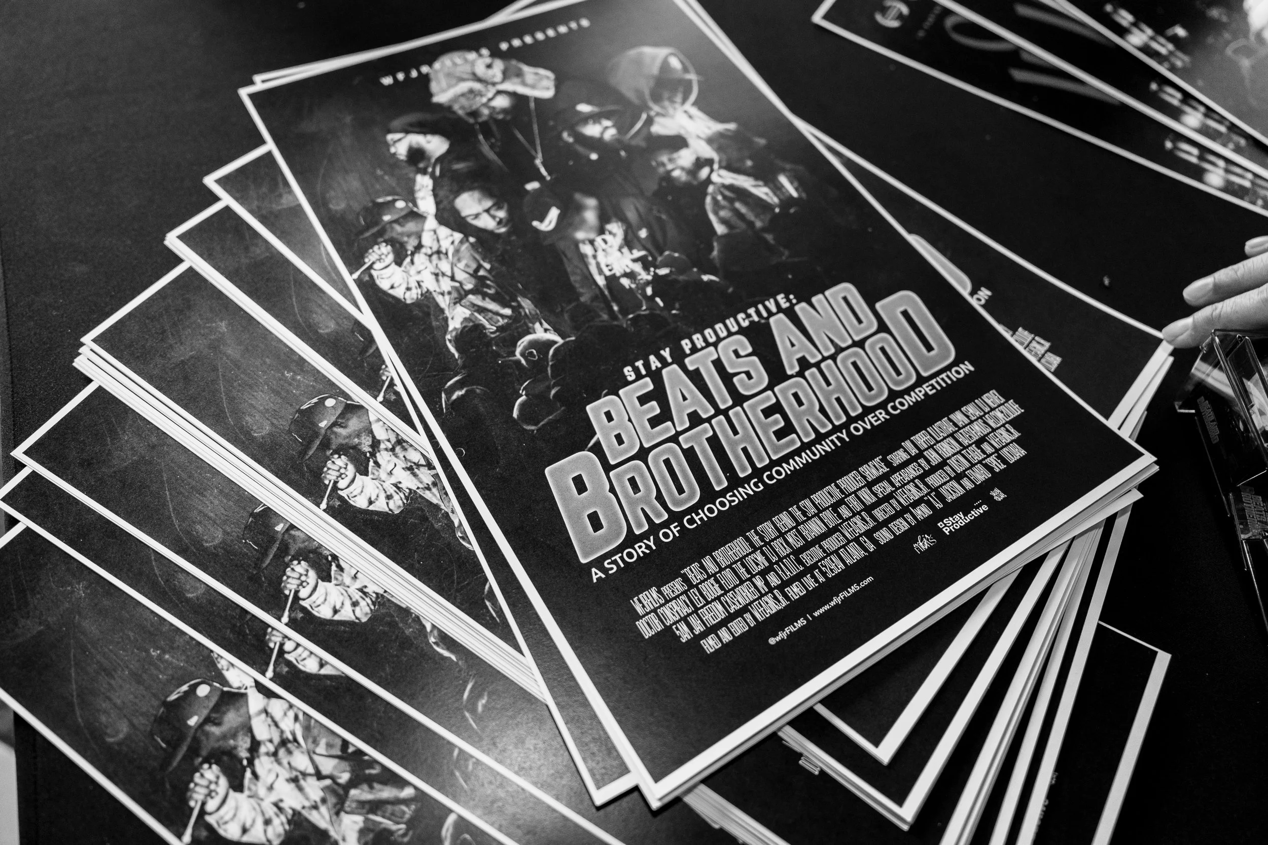 Several black and white posters titled 'Stay Productive: Be As And Bothered', featuring images of people in helmets and casual clothes, stacked on a table, with one person's hand holding a pen cursor at the edge.