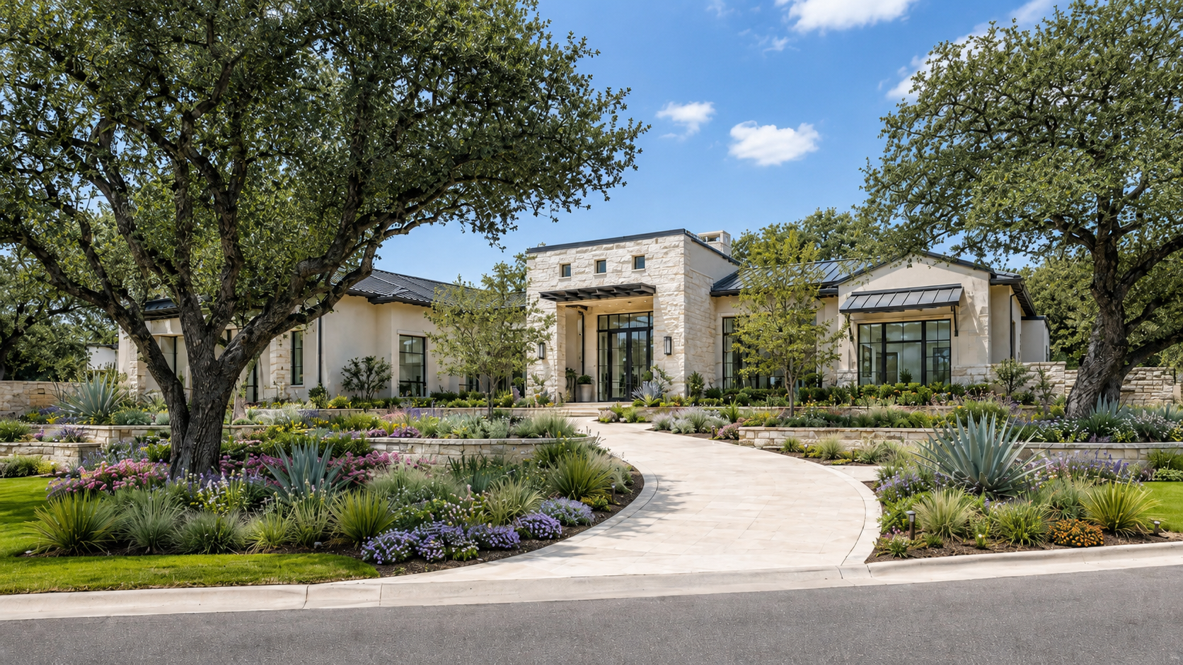Modern house with stone and stucco exterior, surrounded by well-maintained garden with colorful flowers and drought-tolerant plants, large trees, and a curved walkway, under a blue sky.