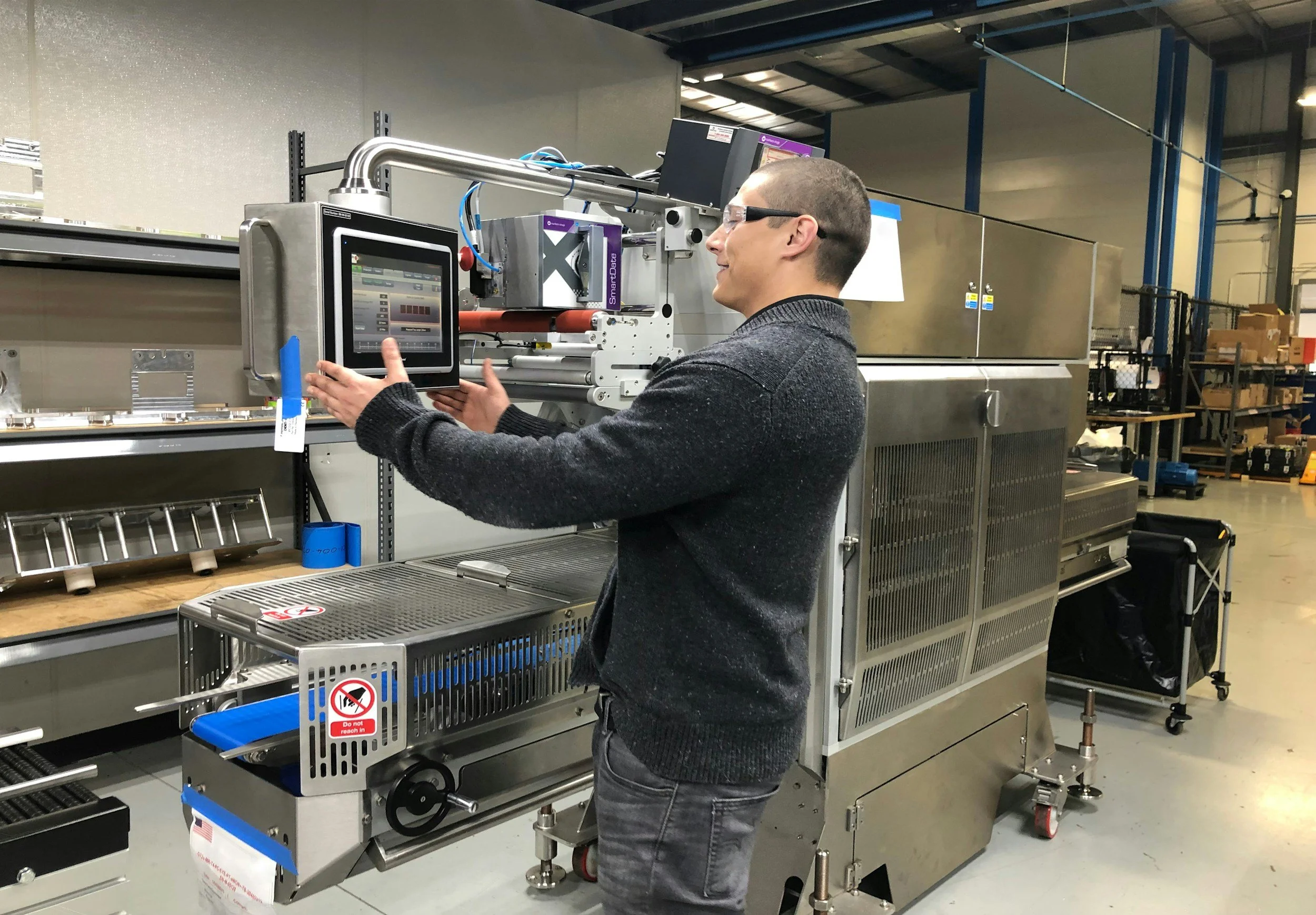 A man wearing glasses operating industrial machinery in a warehouse setting.