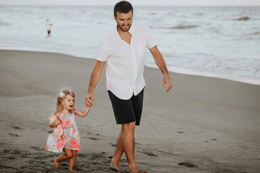 Father and young daughter holding hands walking down the beach