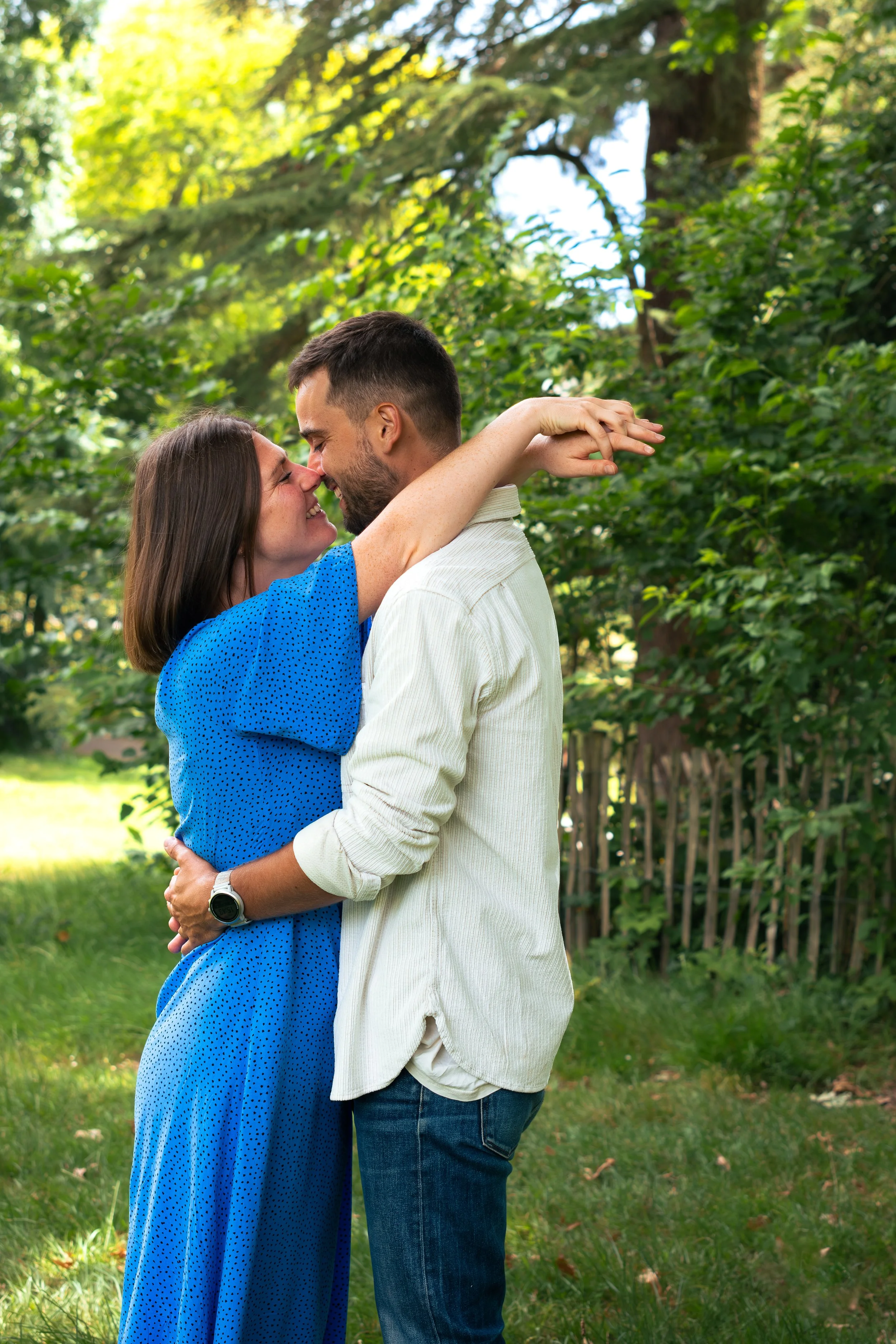 Un couple s'embrasse tendrement dehors dans un jardin verdoyant, en pleine nature, par une journée ensoleillée.