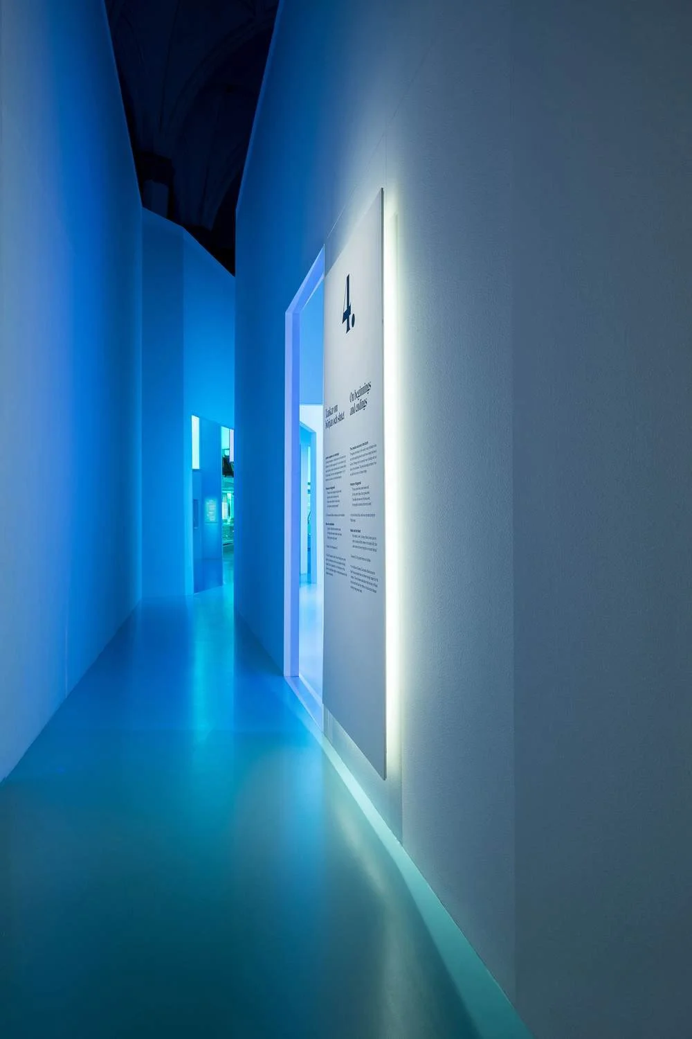 A modern, minimalist hallway with blue and white lighting, featuring informational panels on the walls.