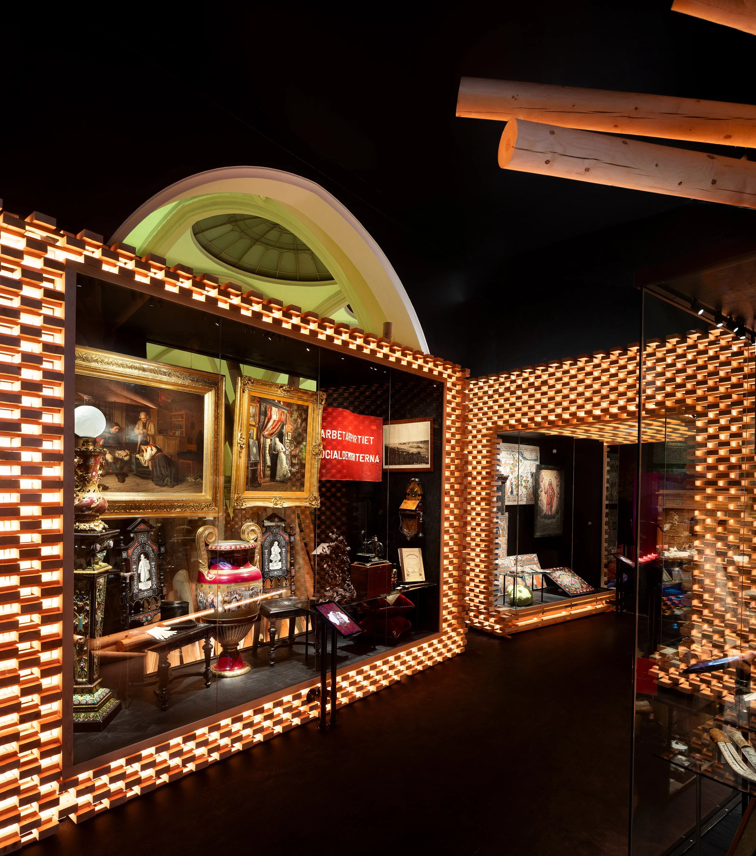 Interior of an art gallery featuring paintings, antique objects, and a display case with jewelry, illuminated by warm lighting and decorated with a unique zigzag patterned frame.