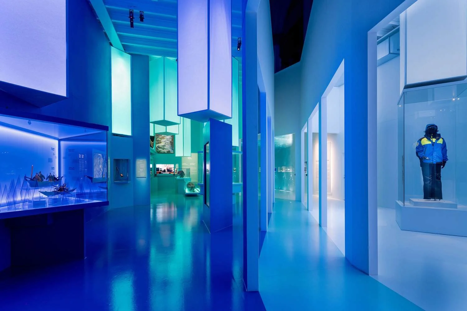 Interior of a modern museum with colorful lighting, displays, and a mannequin in a display case wearing a blue and yellow jacket.