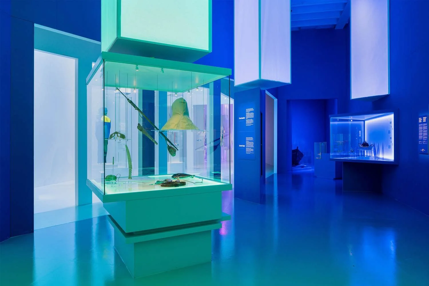 A modern museum exhibit with illuminated display cases containing artifacts, primarily in shades of blue and green.
