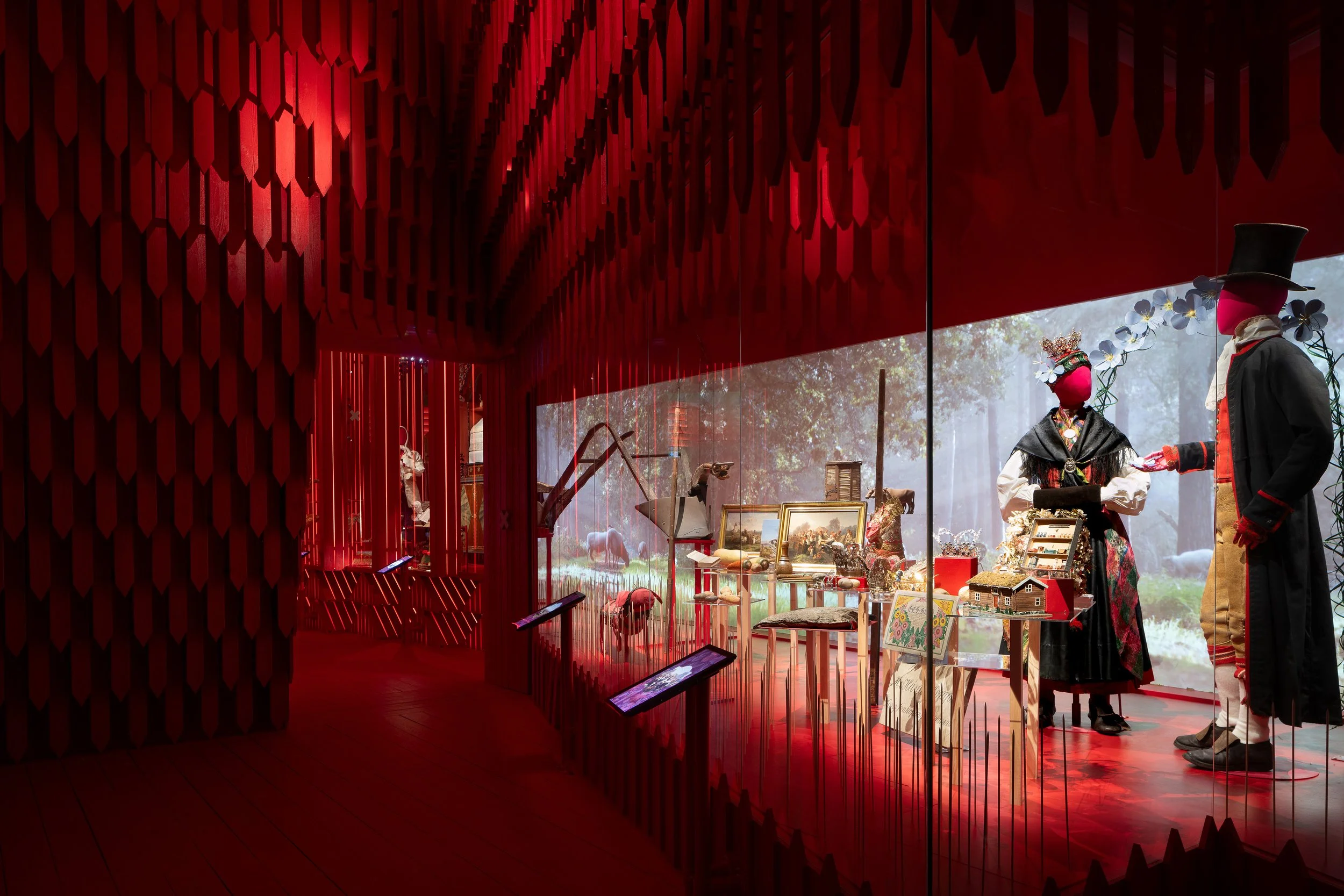 A museum display window with mannequins dressed in traditional costumes and various objects, with a scenic outdoor backdrop.