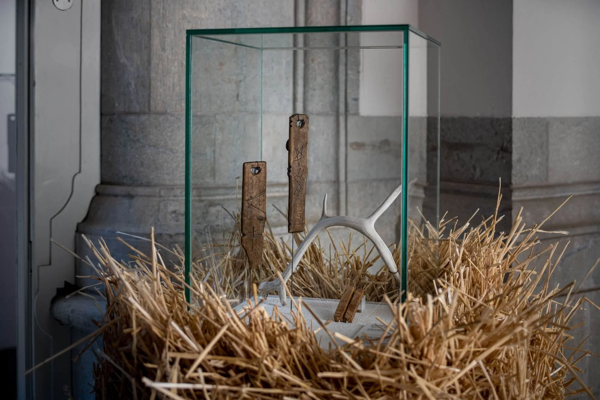 Display case with various historical artifacts including carved bones, sticks, and straw.