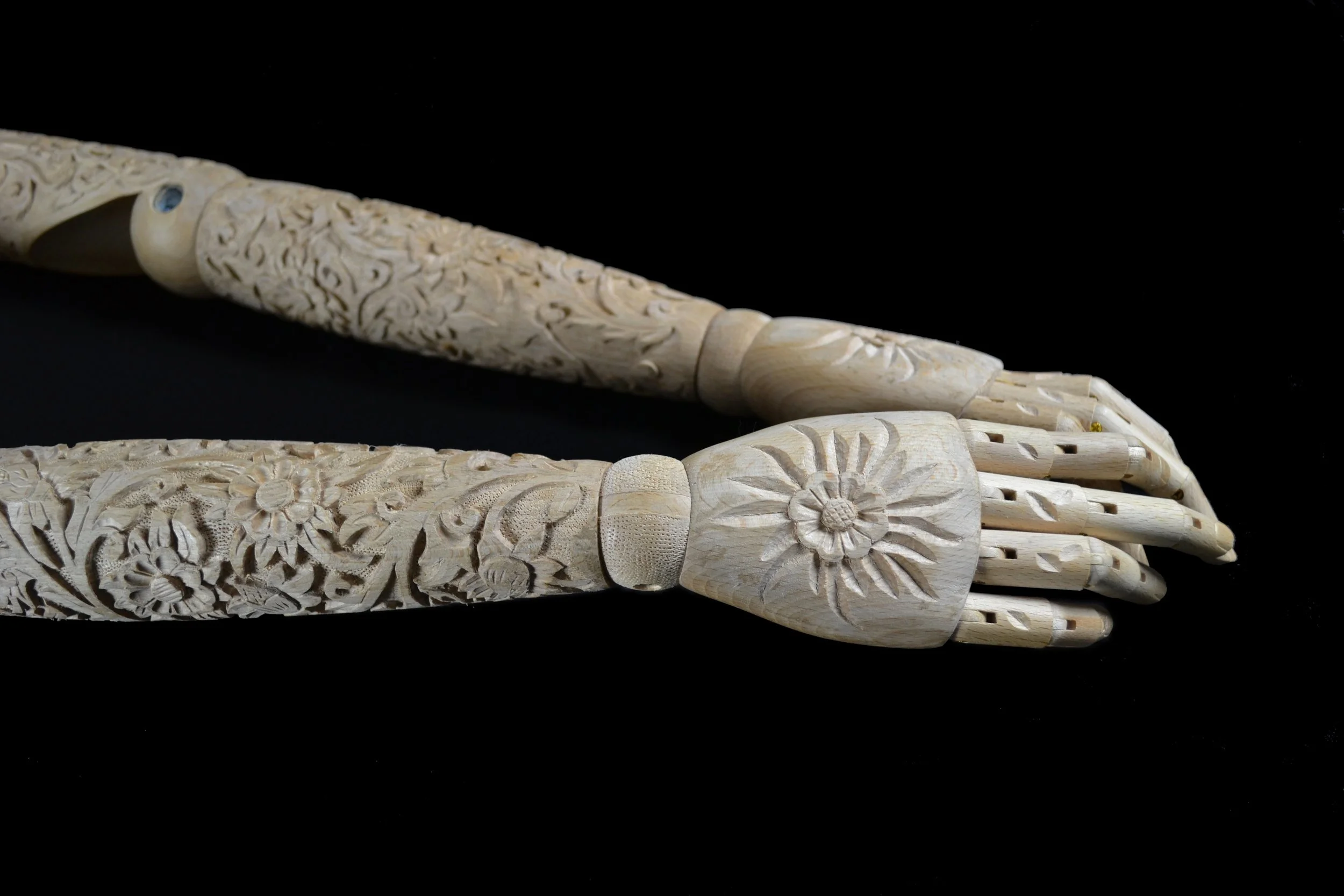 Close-up of an intricately carved mannequin arms with floral and nature motifs, set against a black background.