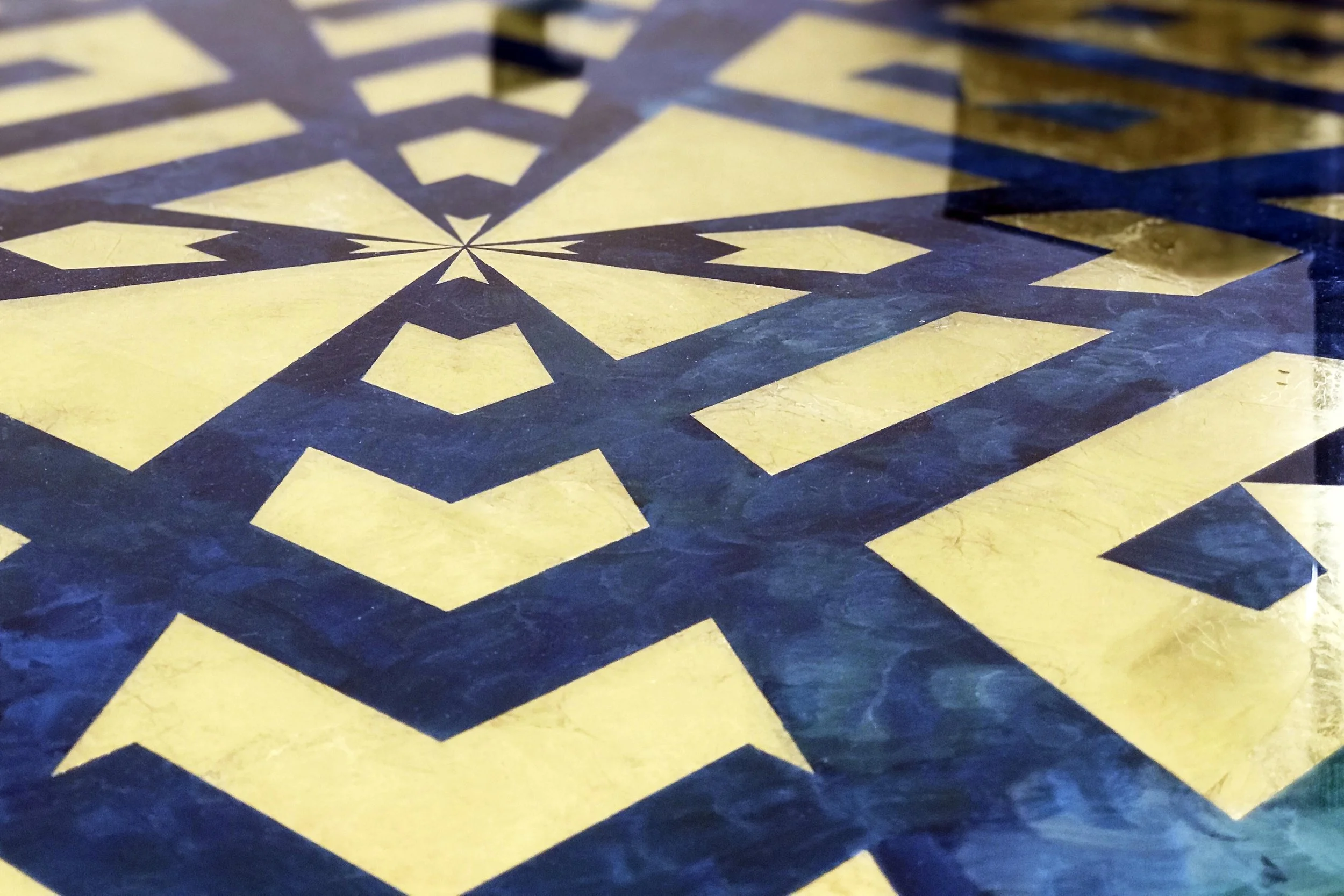 Close-up of a gilded ceiling panel with gold and dark blue geometric shapes and lines.