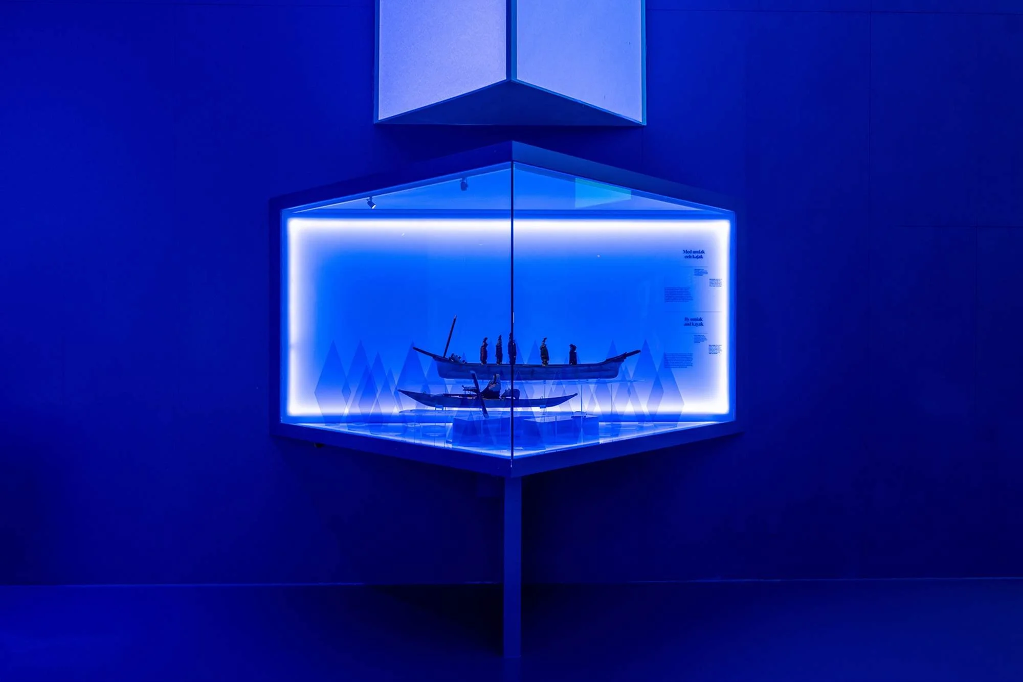 A model ship with multiple sails displayed inside a glass case with blue lighting.