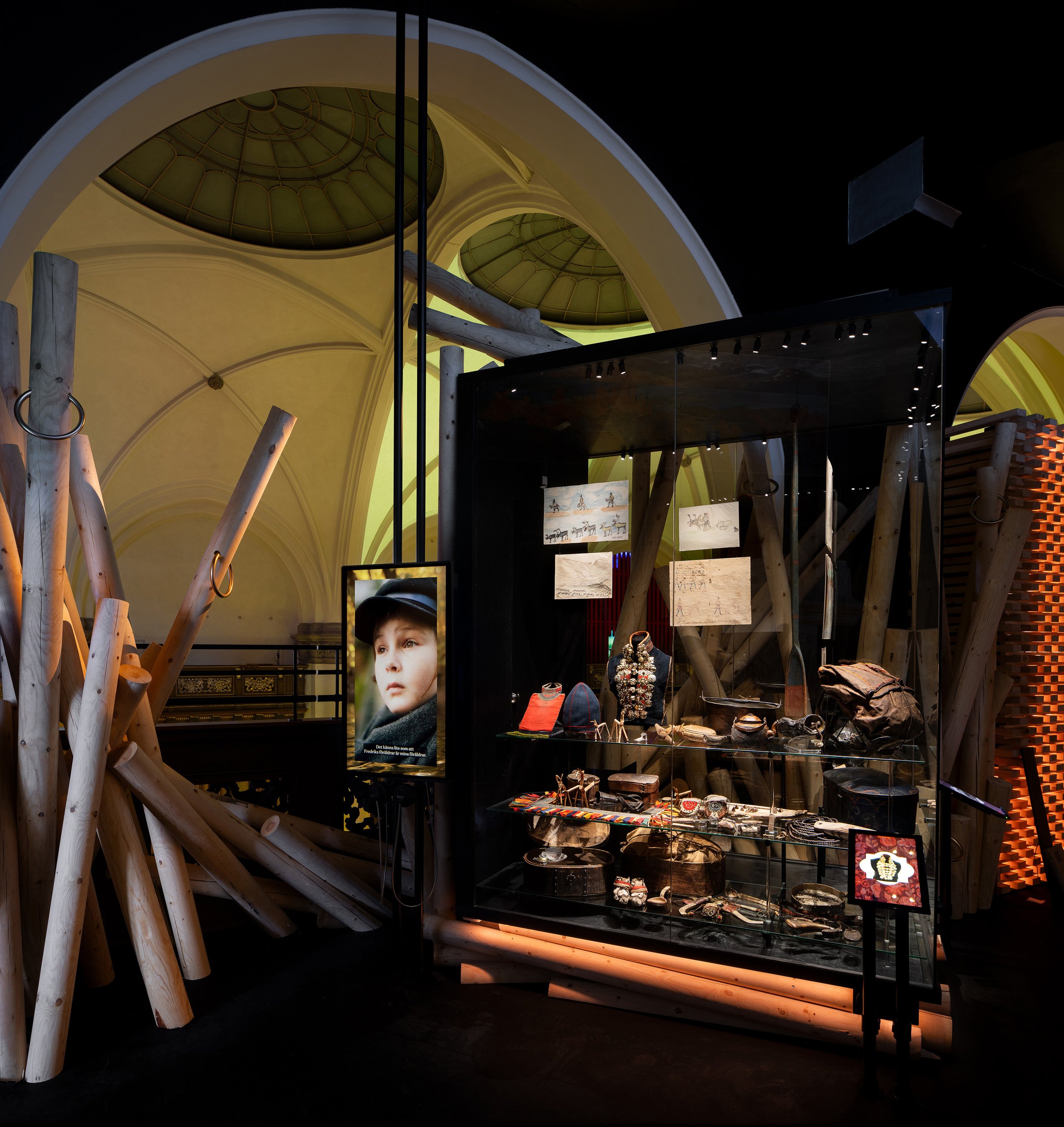 A jewelry store display with various jewelry pieces inside a glass case, set against a background of decorative architectural elements with large, rounded ceilings and wooden beams.