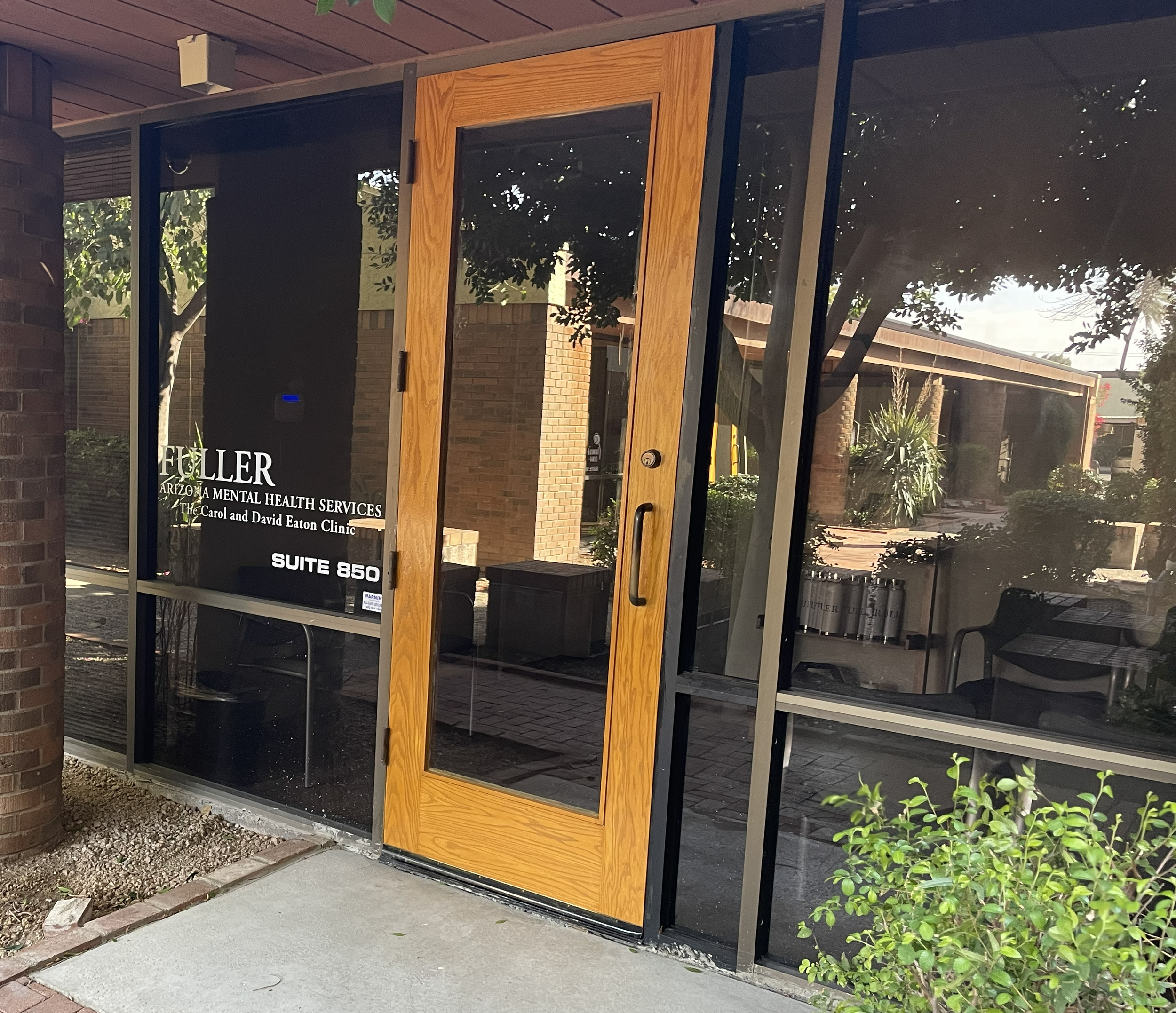 Glass door with wooden frame leading to Fuller Arizona Family Therapy clinic, with trees and plants outside.