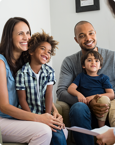 Family of four sitting on a couch during a therapy session, smiling and listening to a therapist.