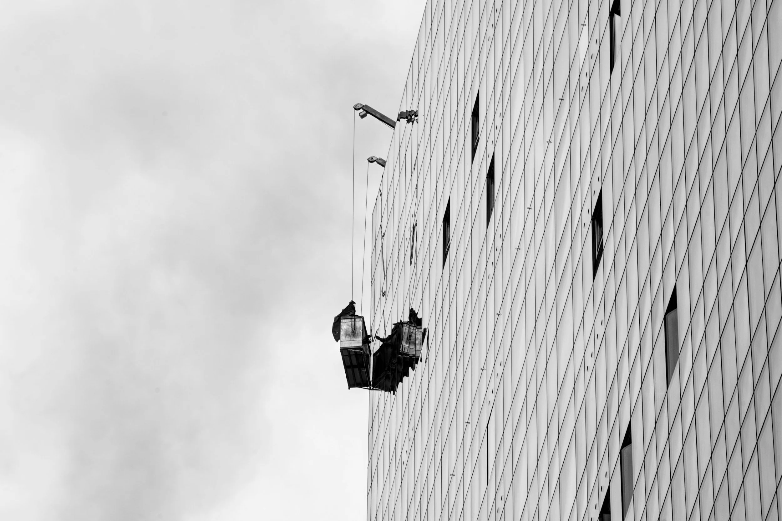 Workers cleaning the exterior windows of a modern glass building on a suspended platform.