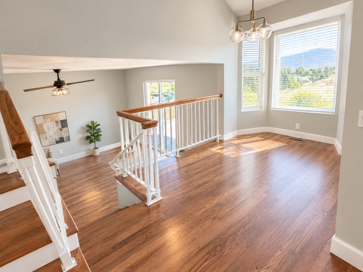 Bright living room with hardwood floors, large windows with blinds, and modern chandelier lighting.