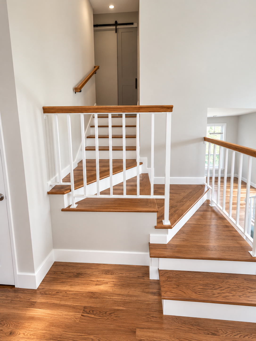 Wooden staircase with white railings and natural wood handrails, leading to a doorway at the top of the stairs in a brightly lit home interior.
