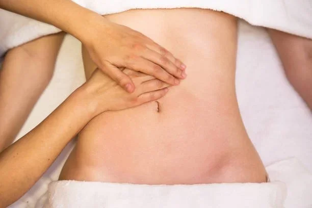 Massage therapist's hands on patient's belly to stimulate lymphatic drainage after plastic surgery.