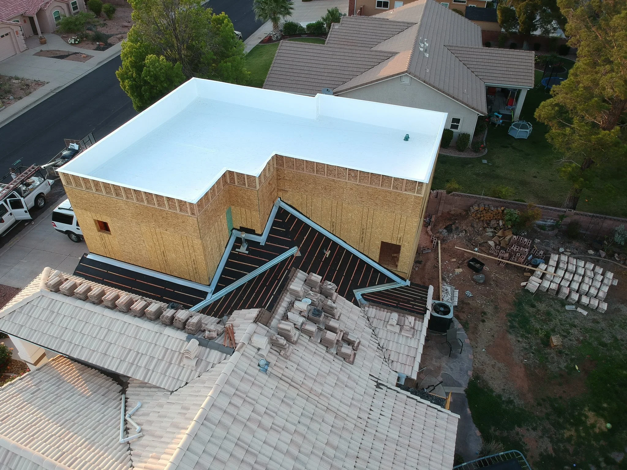 Vista aérea de una casa en construcción con paredes de madera y techo de teja, rodeada de árboles y otras casas en un vecindario.