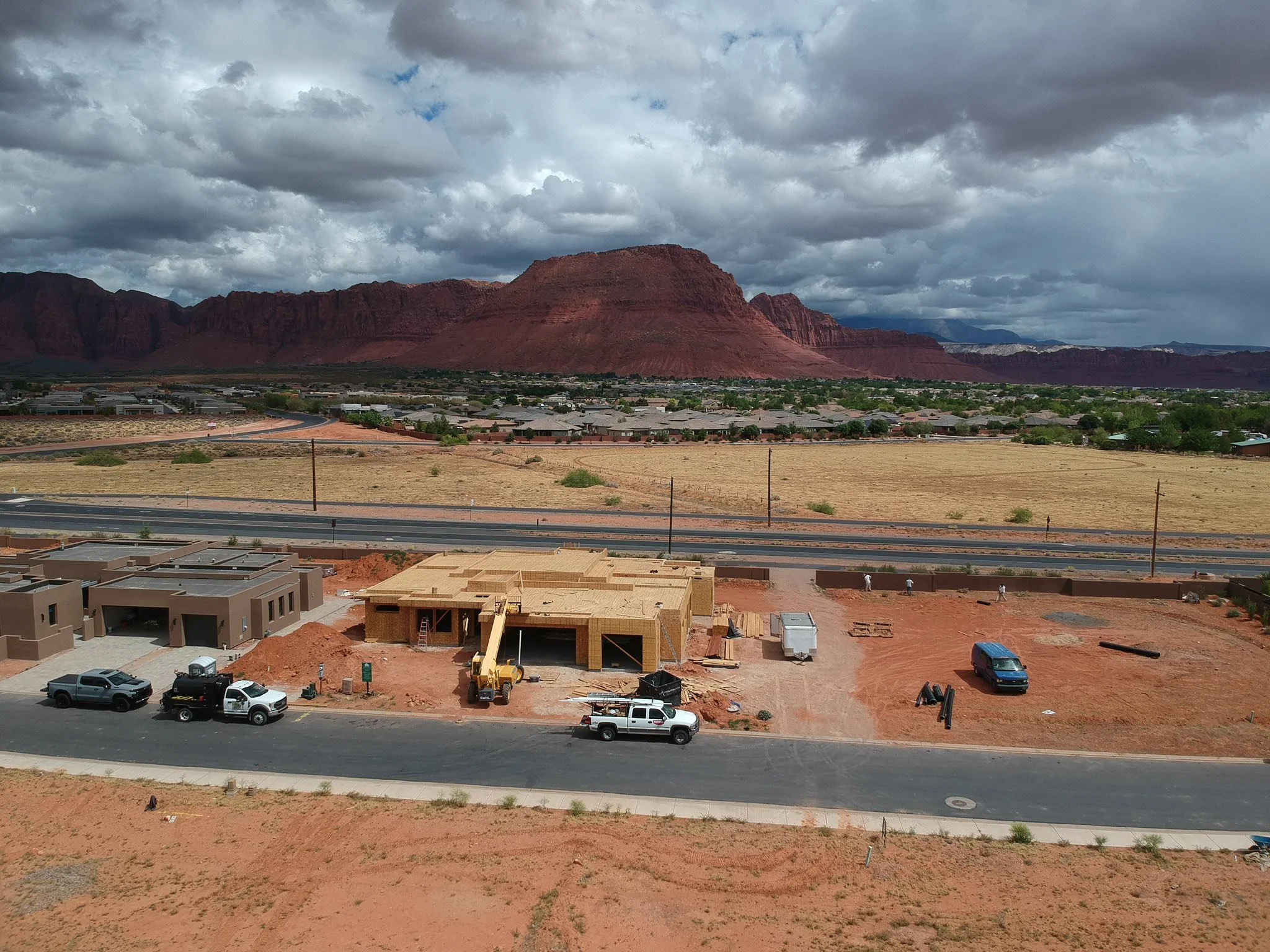 Vista de un área en construcción en primer plano con vehículos y casas en curso, y en el fondo montañas rojas y cielo nublado.