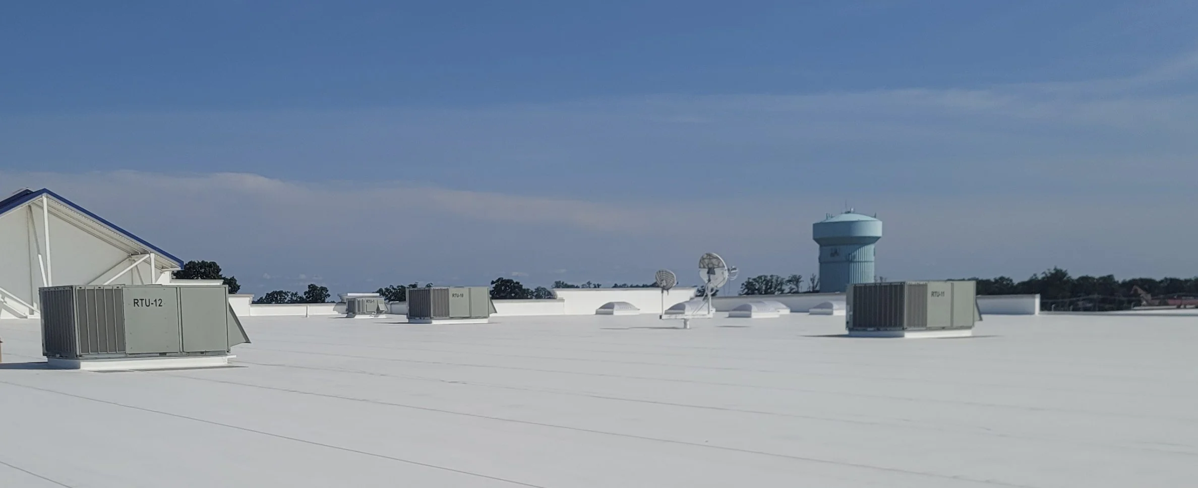 Rooftop with HVAC units, satellite dishes, and a large blue water tower in the background under a clear blue sky.