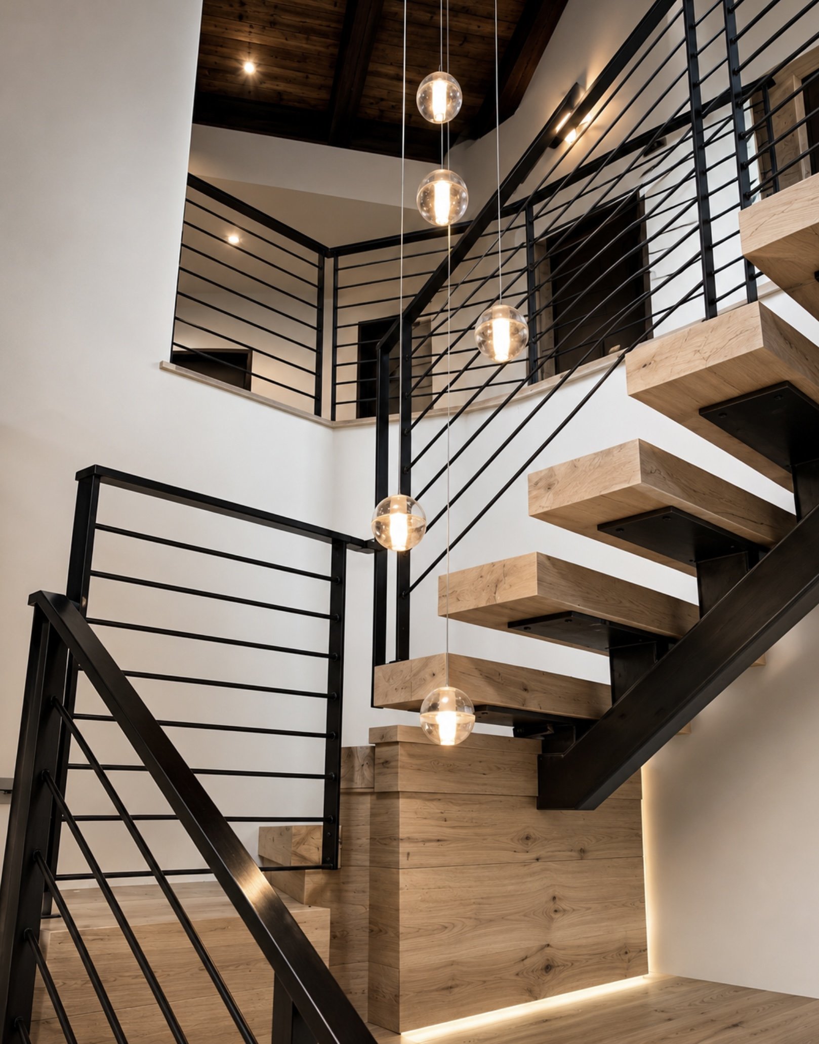 Modern staircase with wooden steps, black metal railing, glass pendant lights, and a wooden ceiling.