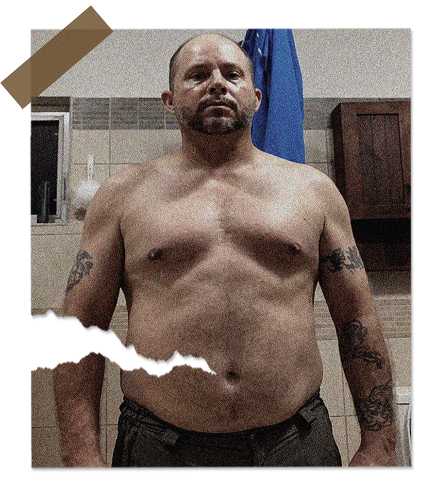 A shirtless man with tattoos poses in front of a bathroom mirror.