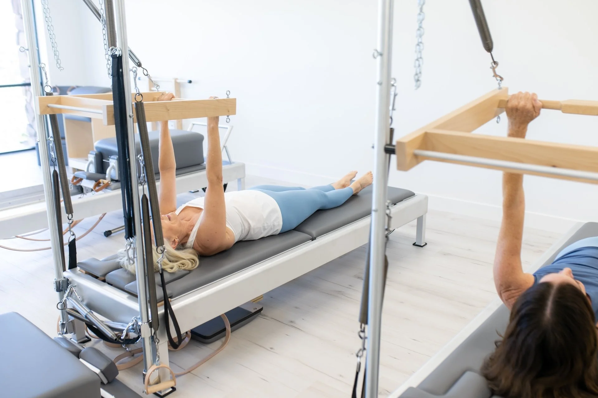 Two clients performing synchronized Pilates reformer exercises in guided session