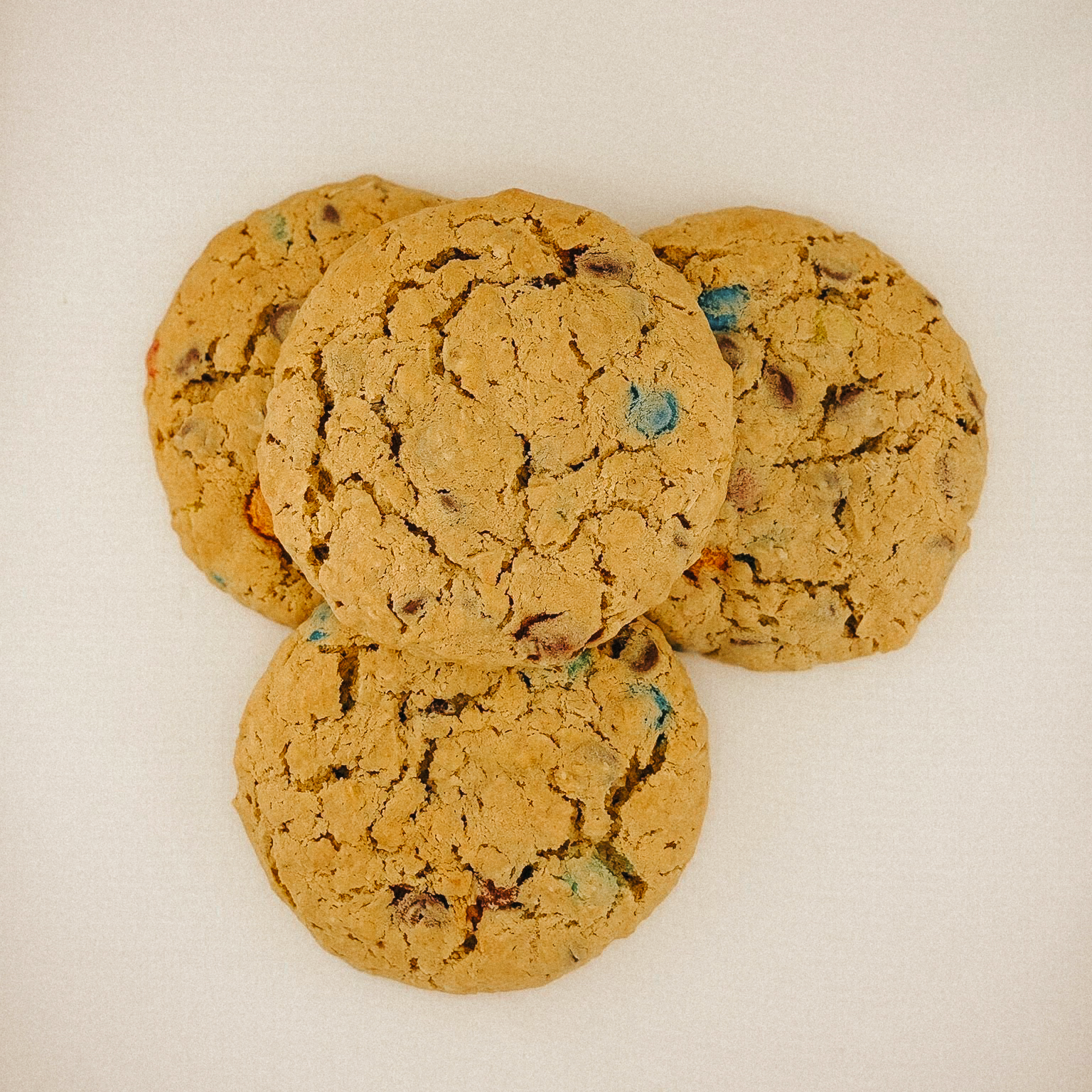 Four chocolate chip cookies with colorful candy pieces on a white surface.