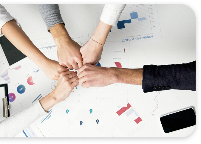Cuatro personas haciendo un gesto de unión con las manos sobre una mesa con gráficos y documentos de negocios.